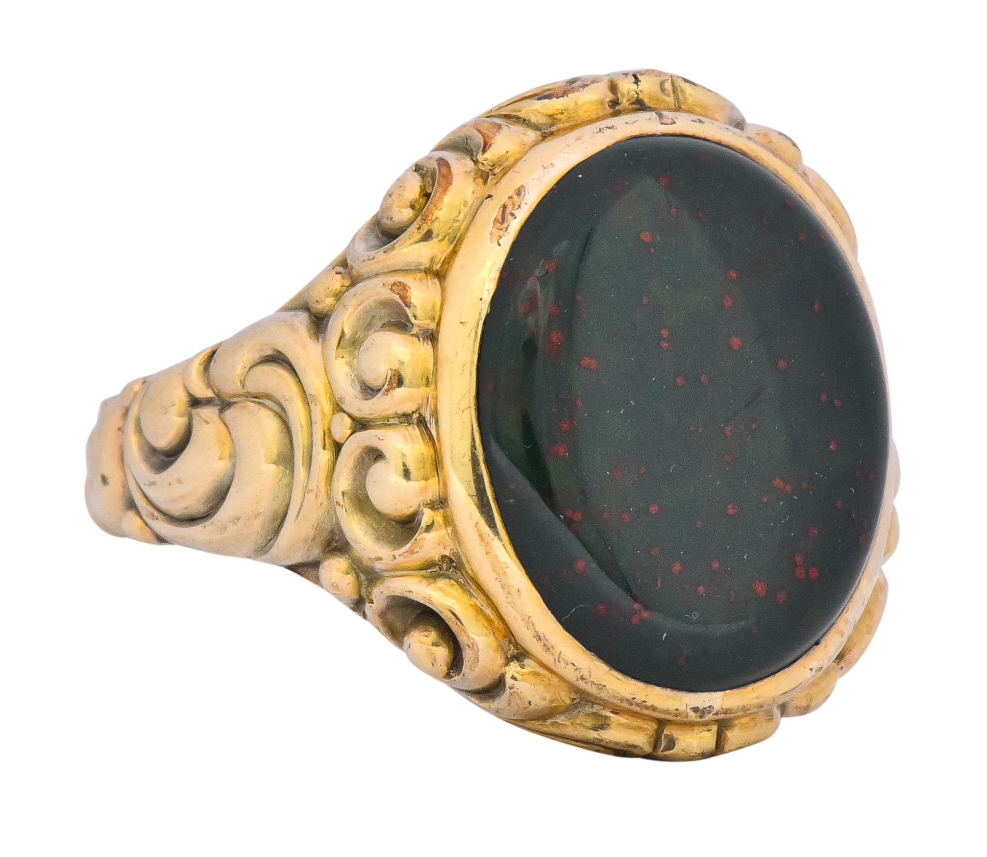 Centering an oval flat polished cabochon bloodstone, measuring approximately 17.0 x 14.7 mm, deep green and flecked with red

Bezel set in high polished gold

With scrolling gold work upon gallery and down the shank

Maker's mark and stamped 333 for