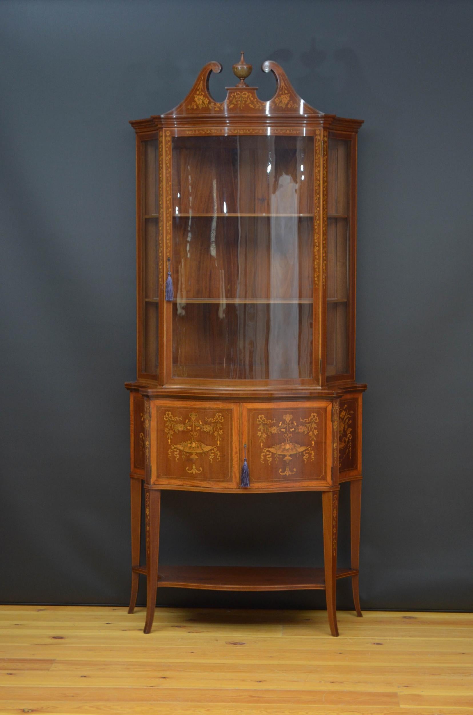 Sn4956, a Sheraton revival, mahogany and marquetry display cabinet of serpentine design, having finely inlaid swan neck pediment with a finial to center, cavetto cornice above a glazed door fitted with original working lock and a key above a
