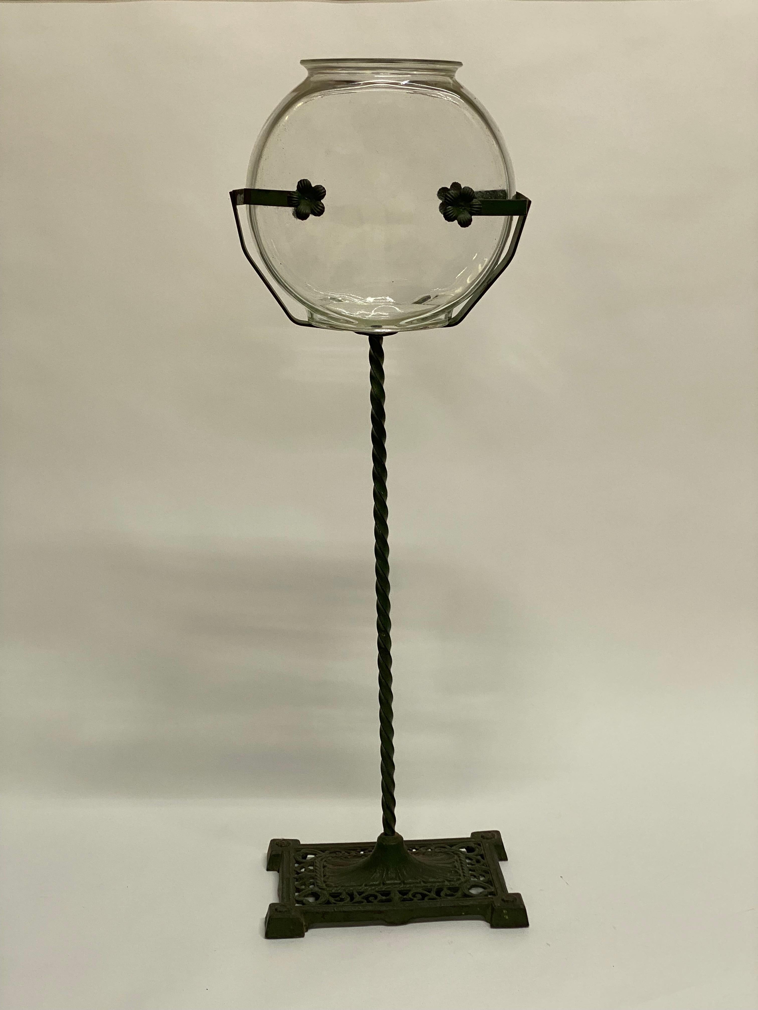 Late Victorian fish bowl or terrarium. Rope twist stem, skeletal strap holder with cut out floral motif on a pierced scroll decorated base, circa 1890-1920. Green painted iron stand. Good overall condition with no visible chips or cracks to the