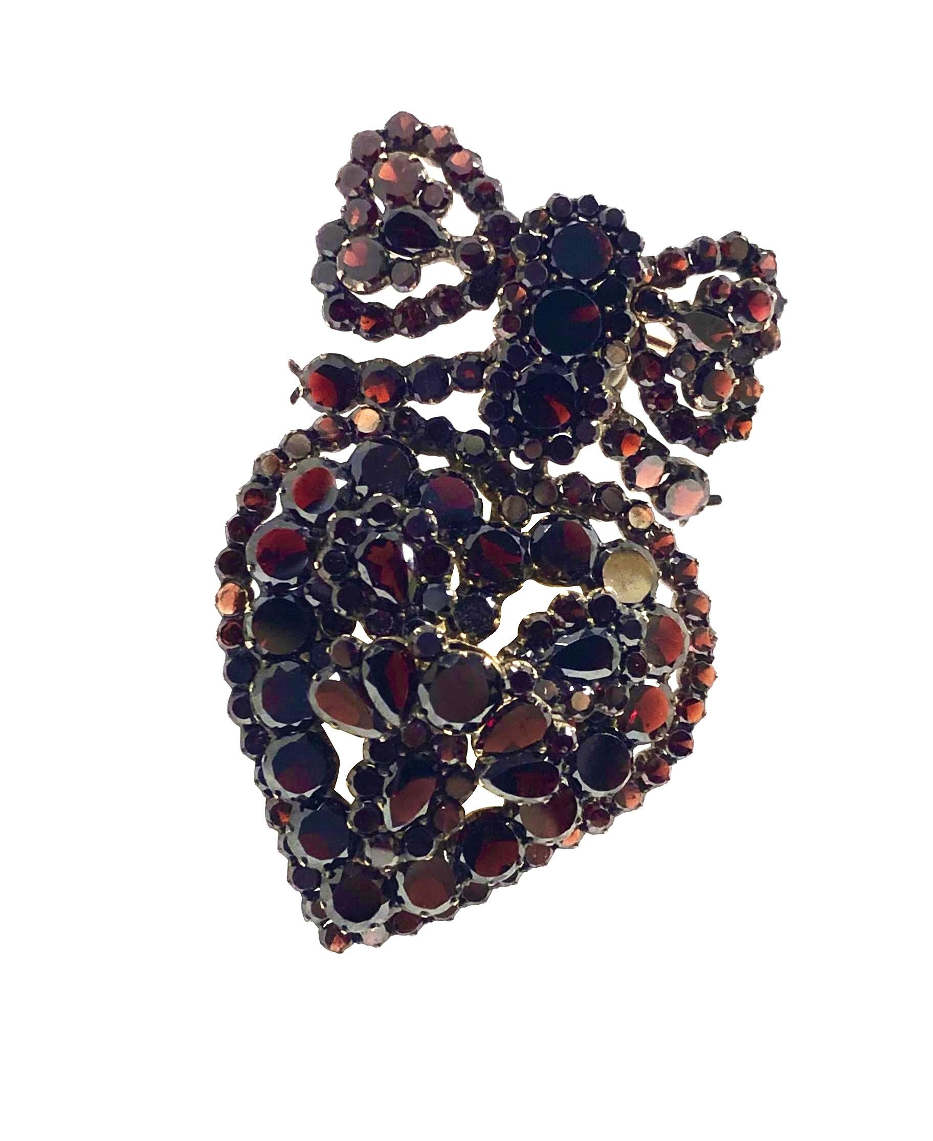 Circa 1900 - Pendentif en métal doré en forme de cœur avec un nœud de broche attaché, mesurant 2 1/4 pouces de longueur et 1 1/2 pouces de largeur, serti de grenats de Bohème, ronds et en forme de poire, le dos du cœur a un compartiment couvert de