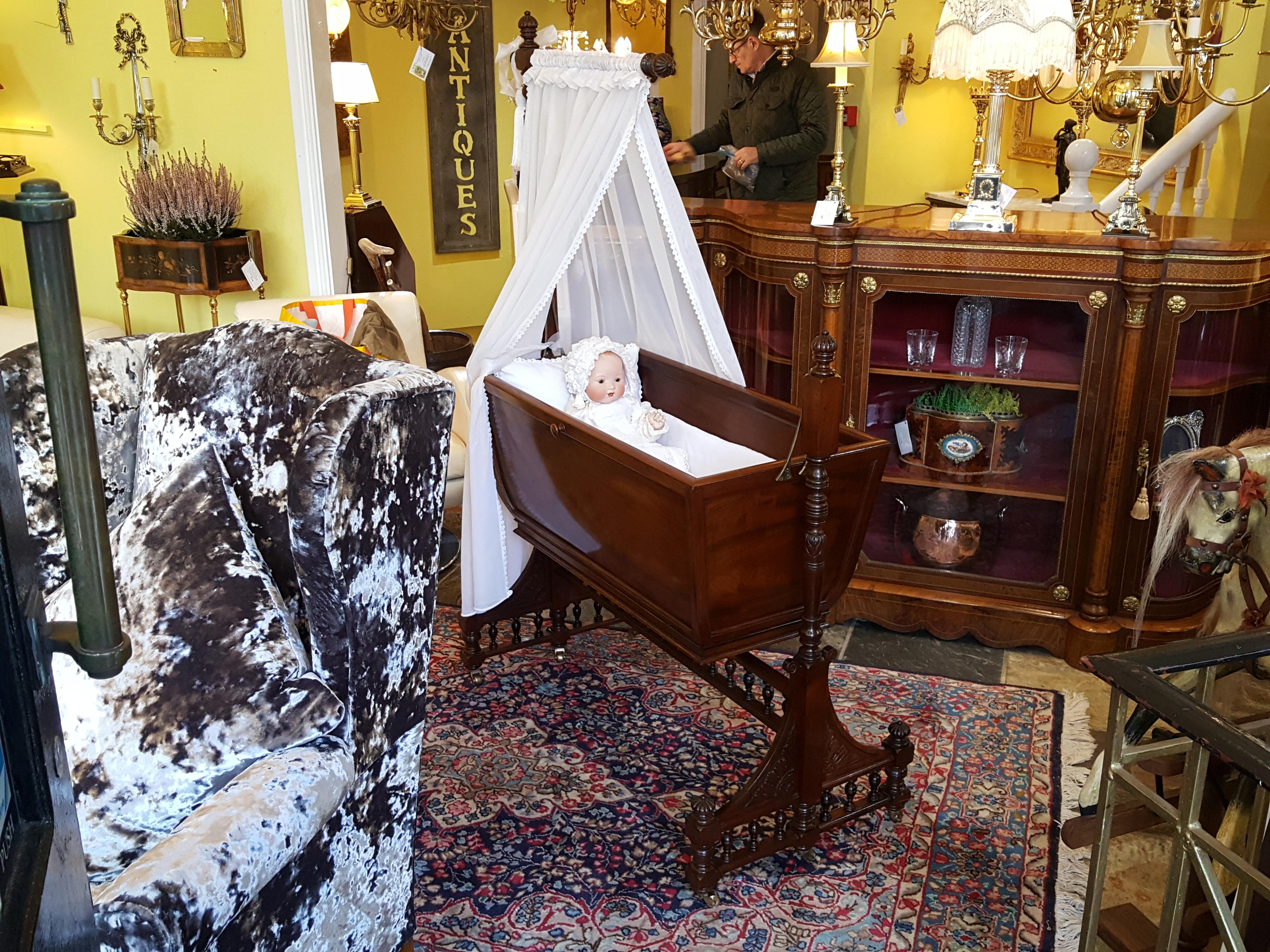 Late Victorian mahogany cot, the crib veneered with a flame mahogany with frieze, turned frame with gadrooned finials, bobbin turned spindles to the stretcher and brass castors - attributed to Gillows of Lancaster. Measures: 42