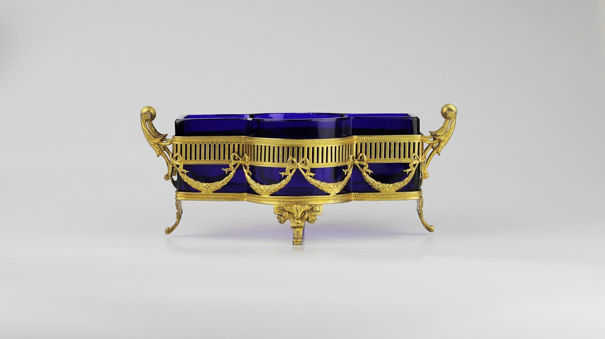 An impressive gilt sterling silver footed basket with original cobalt blue glass liner. The silver frame sits upon four gilt sterling feet and externally features swags with bows and neoclassical style detailing. The inside of the gilt silver basket