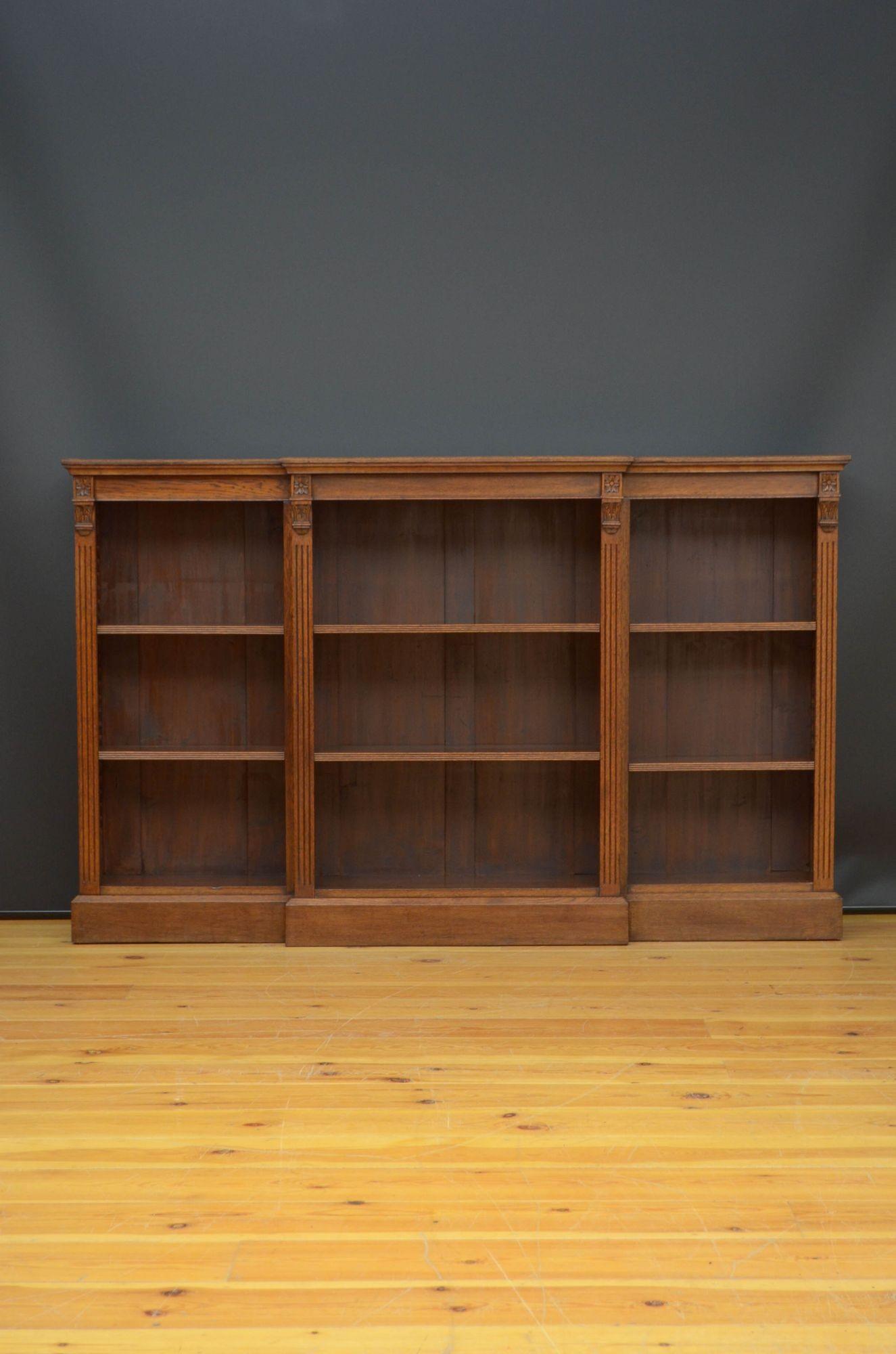 Sn5380 Late Victorian, break fronted open bookcase in oak, having oversailing top above projecting centre section and further two open sections, each with two height adjustable shelves, all standing on plinth base. This antique bookcase retains its