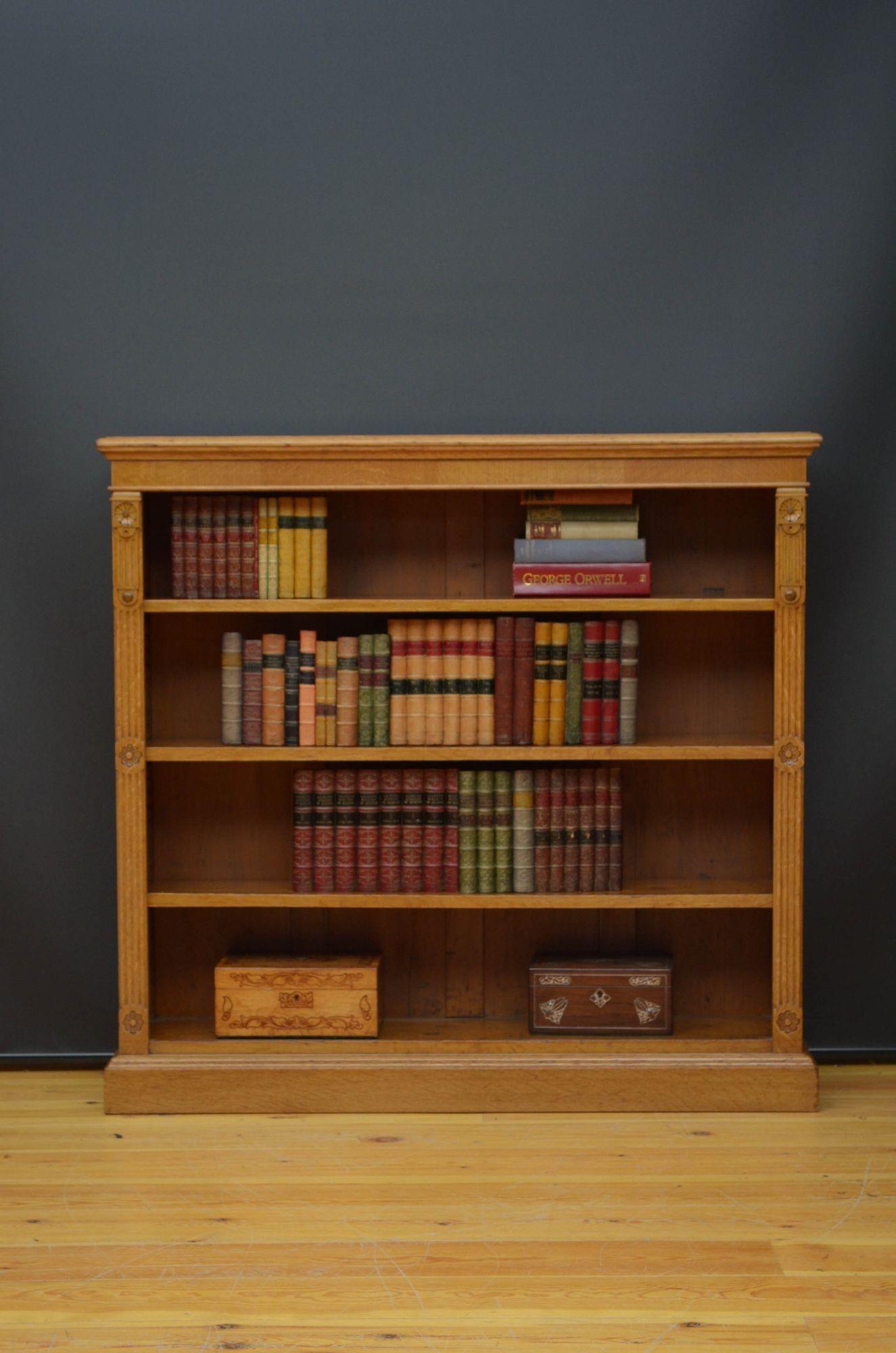 St040 Late Victorian open bookcase in oak, having oversailing top with moulded edge above three height adjustable shelves, all flanked by reeded pilasters and carved pateras, all standing on plinth base. This antique bookcase is in home ready