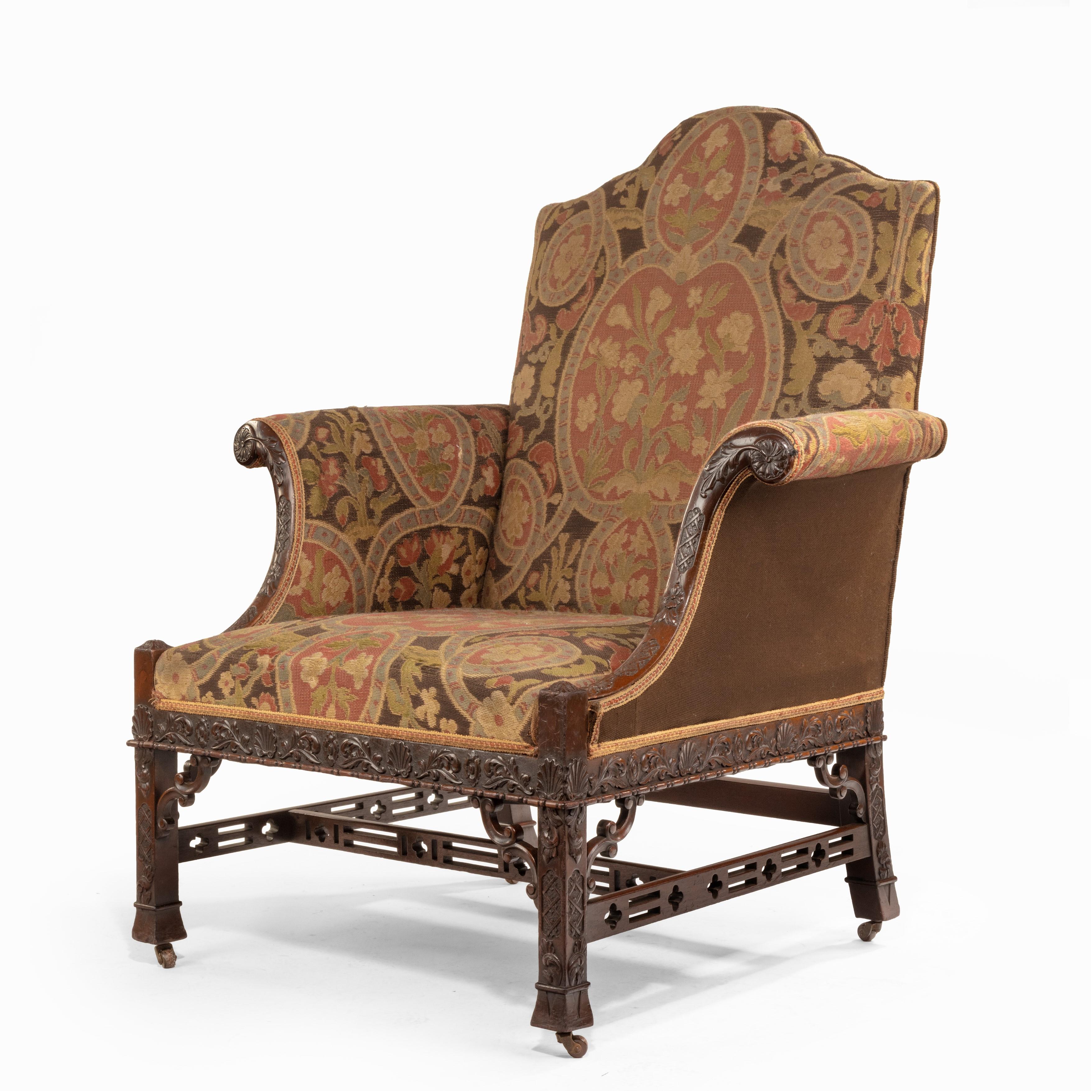 A late Victorian oversized armchair in the Chippendale manner, the scrolling mahogany arms, seat rail and legs carved with scrolling tendrils and anthemion heads, with double C-scroll spandrels and pierced stretchers, with the original needlework