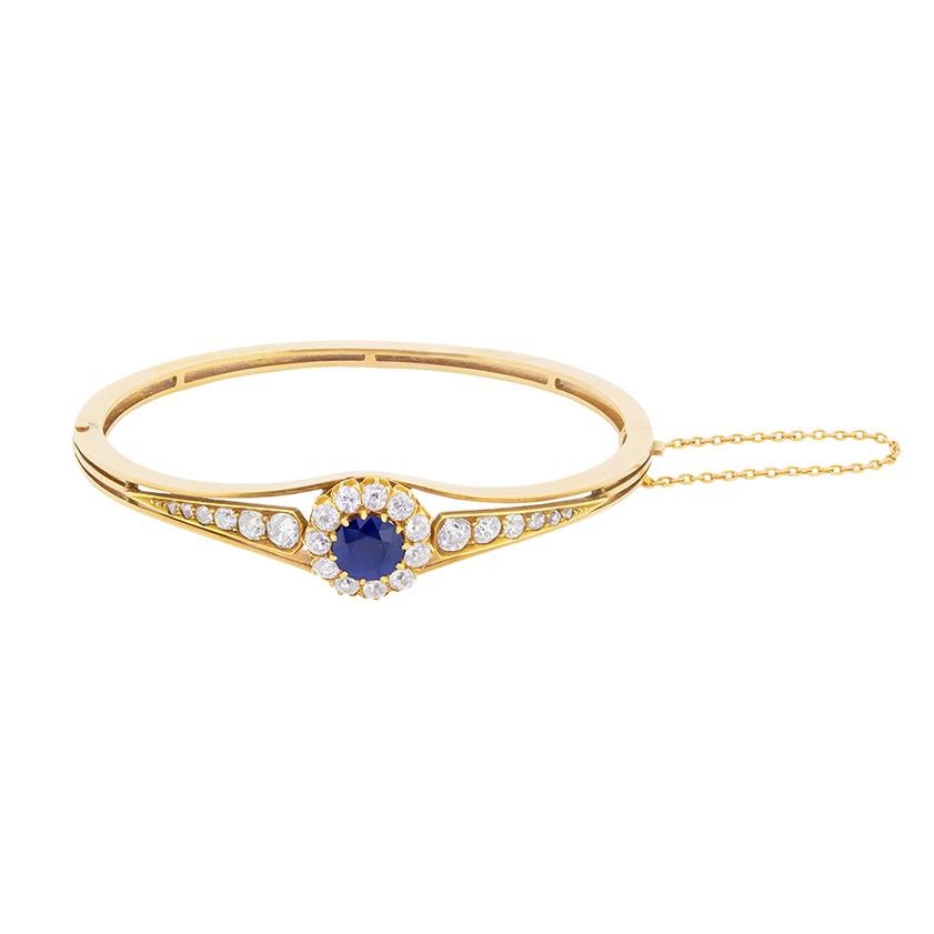 An old cut sapphire surrounded by a halo of old cut diamonds is the centrepiece of this late Victorian era bangle bracelet. The Sapphire weighs 1.80 carat and is a wonderful deep blue. The diamonds, which dazzle with their colour, estimated f and