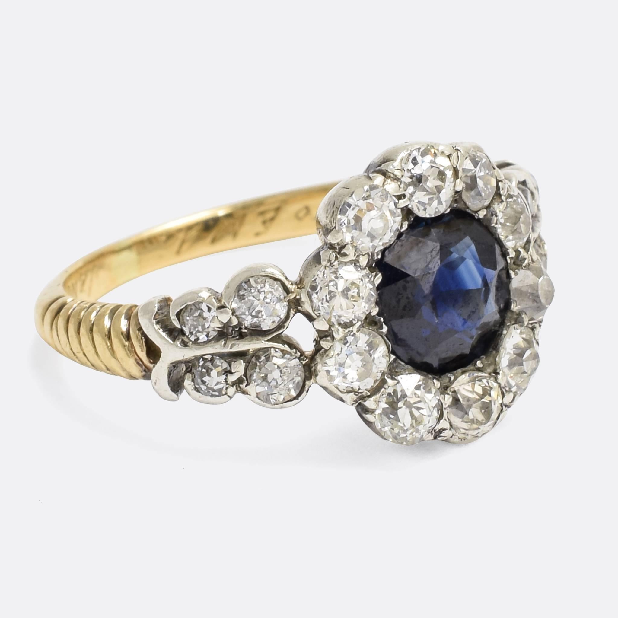 A superb antique cluster ring, set with a central blue sapphire and around three quarters of a carat of bright old mine cut diamonds. Modelled in 15k gold with silver settings, the shoulders are each accented with four diamonds, and the band