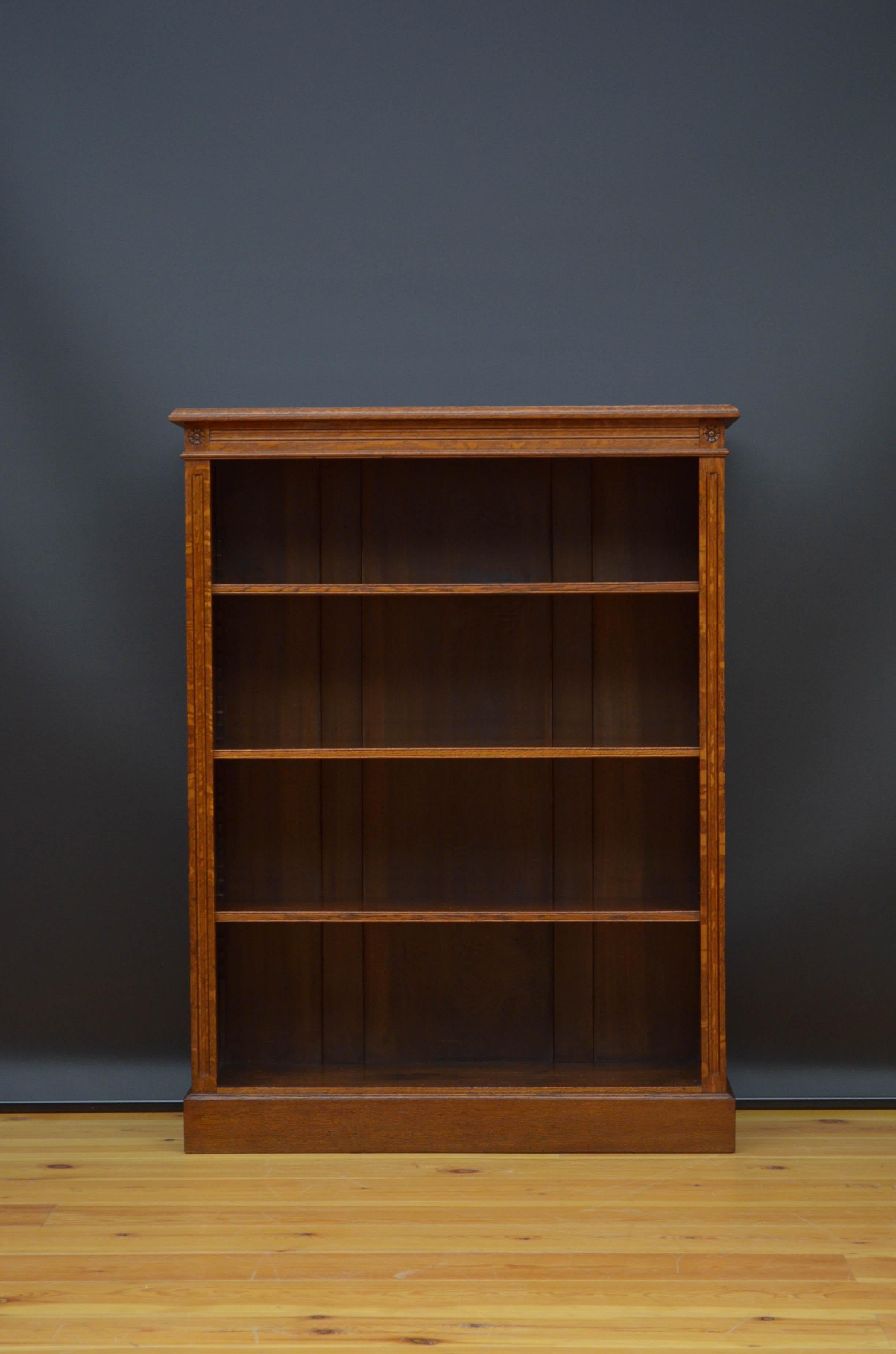 J04 Late Victorian open bookcase in solid oak, having oblong top above reeded frieze with carved paterae and three height adjustable shelves flanked by reeded pilasters, all standing on plinth base. This antique bookcase has been syamthetically