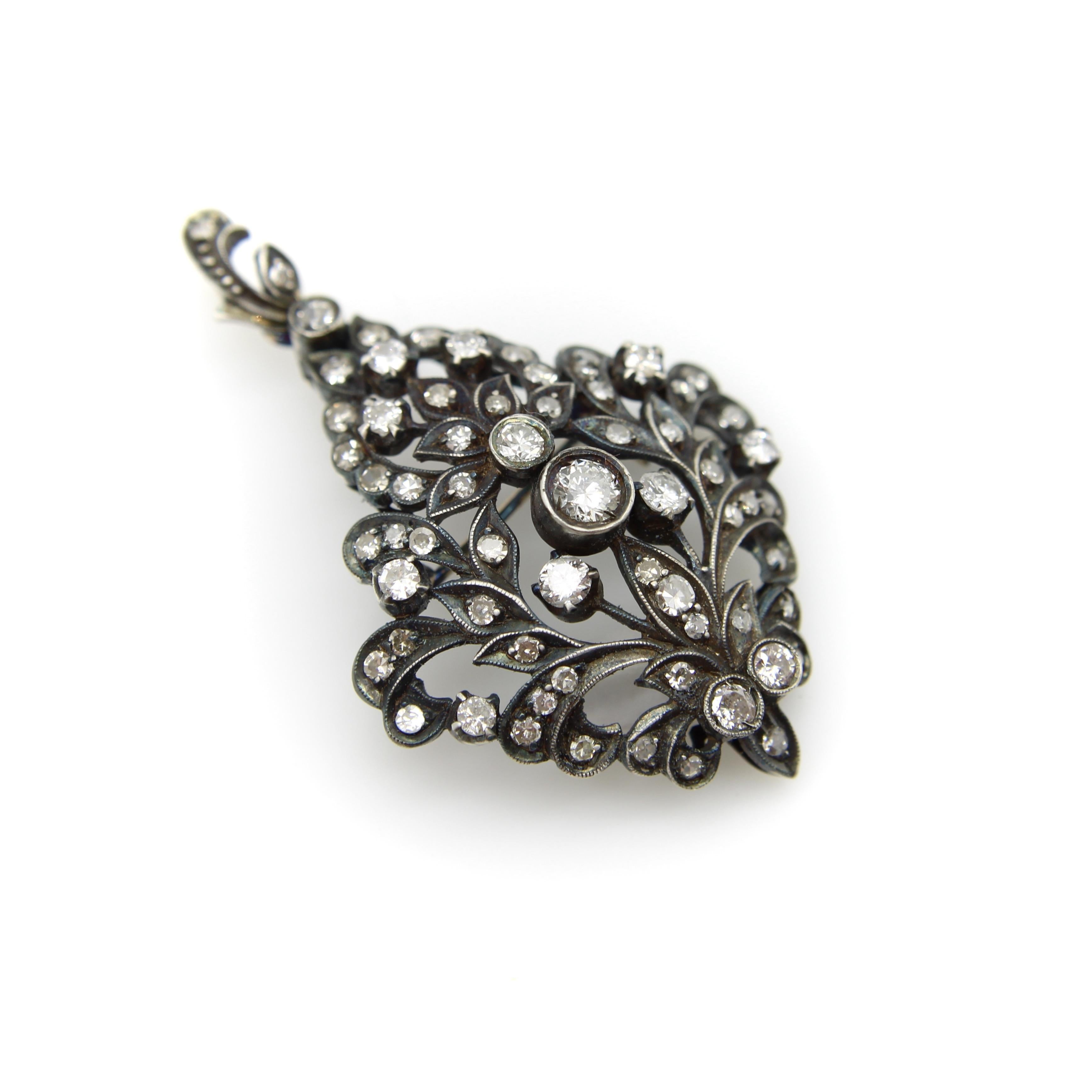This is a stunning late Victorian era 12k gold and sterling silver diamond pendant brooch. This piece has an eye-catching, fanciful design that incorporates diamonds of different sizes, cuts, and clarity. The floral and foliate motif swirls and