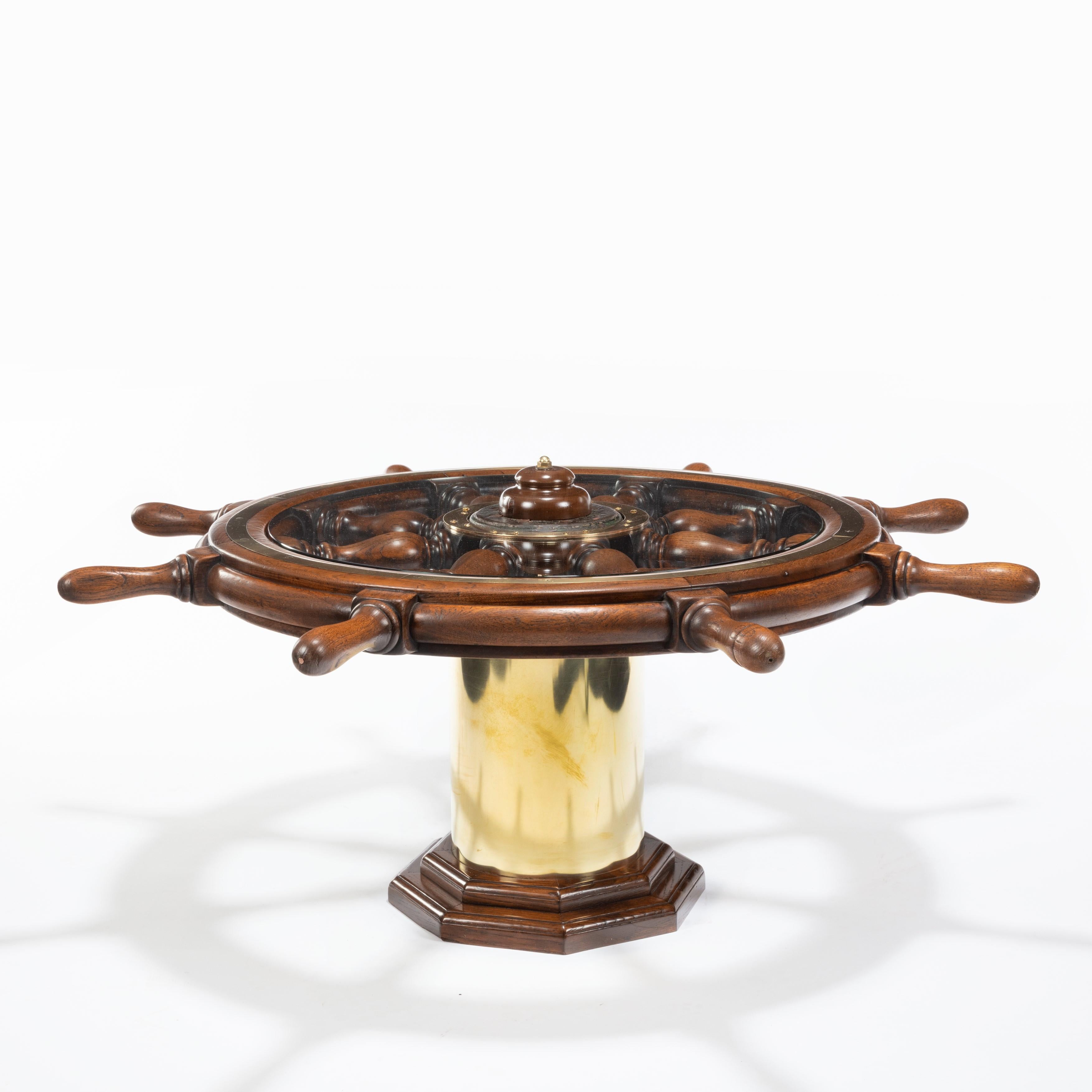 A late Victorian teak steering wheel, raised on a later brass cylindrical base and inset with a glass top to form a coffee table. English, circa 1900.
     