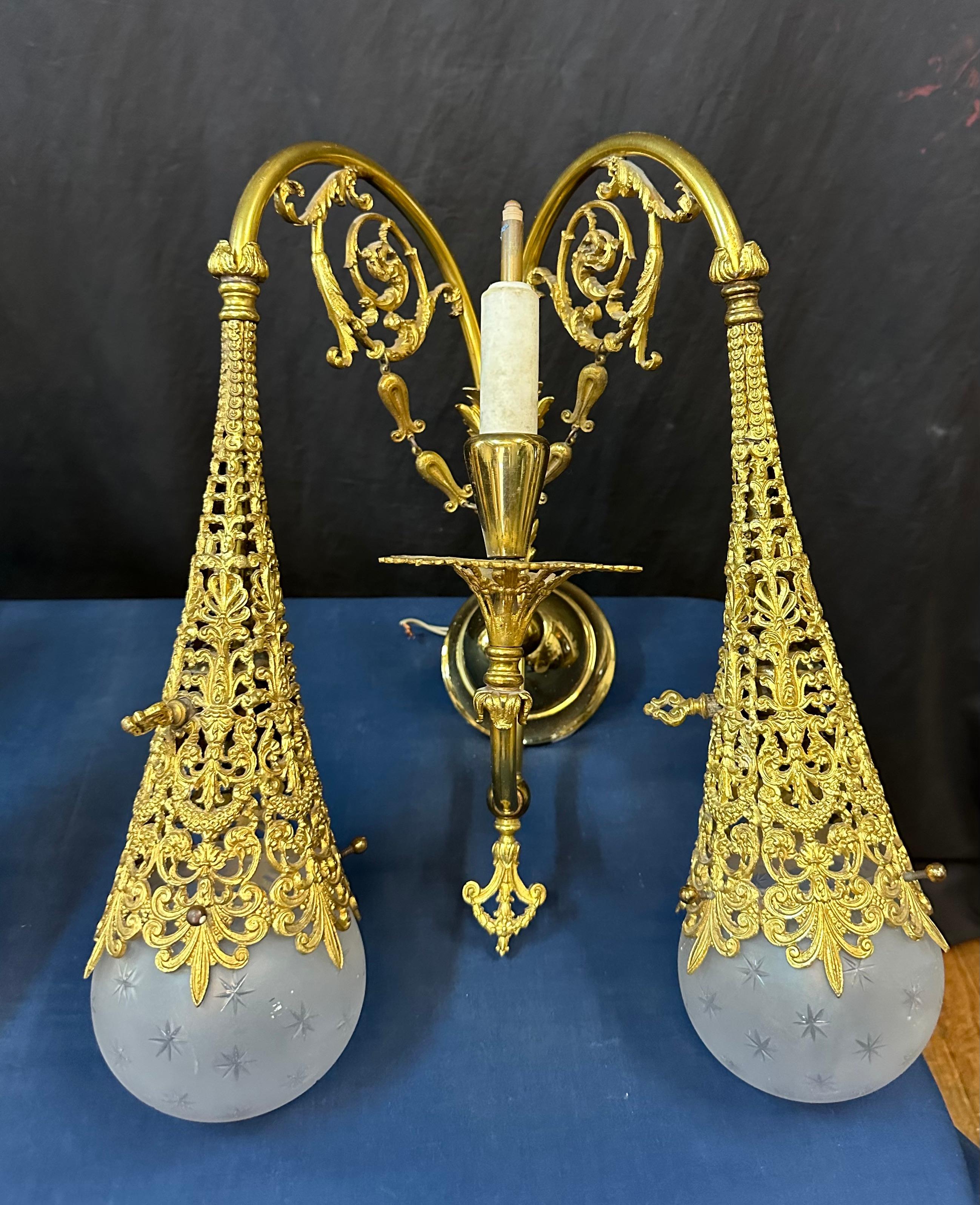 Este elegante par de apliques de latón de finales de la época victoriana están bellamente diseñados con un detallado motivo de filigrana esculpida maciza.... Cada candelabro presenta dos conos de filigrana de latón de diseño elaborado, cada uno con