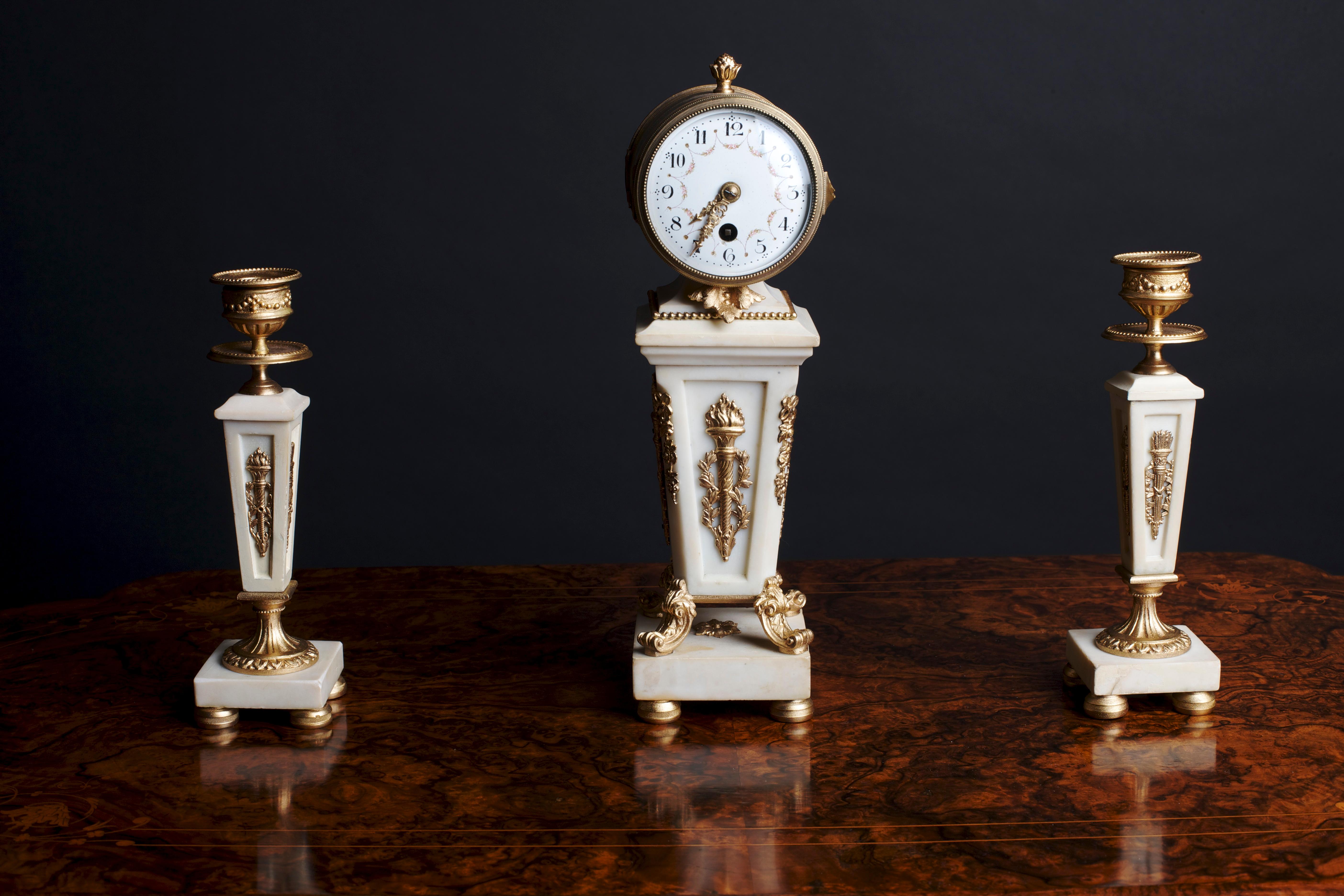 Late Victorian white marble and bone miniature garniture.

The French drum movement with platform escapement supported by a white marble base in the form of an obelisk with gilded mounts and standing on four bun feet. 

 The side pieces with