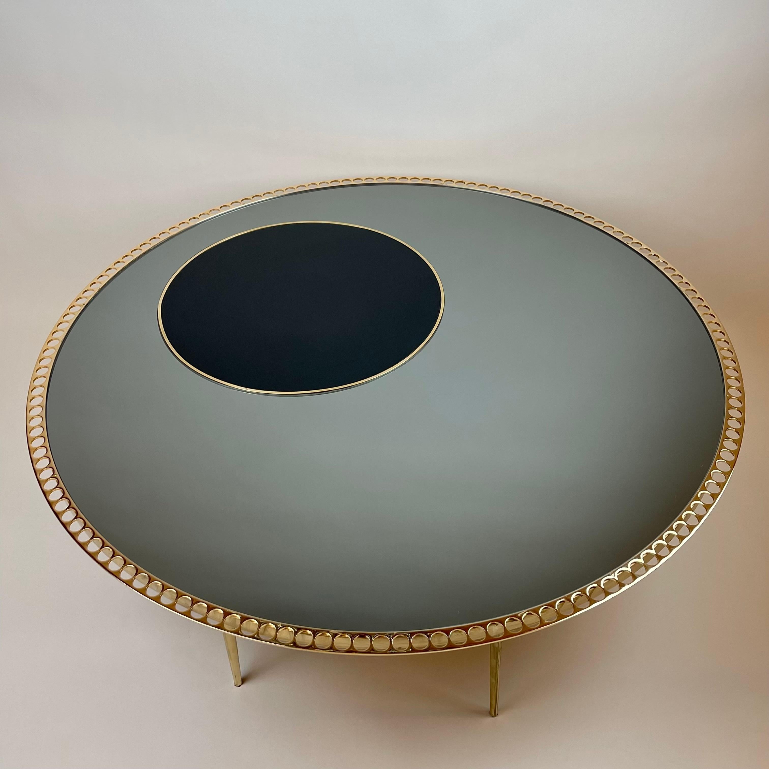 The coffee table has an insert of a black opaline glass dot of 50 diameter cm. on the top, morever it has six solid triangular brass legs & details. While the external holed metal ring of the coffee table is gilded to enhance contrast with the