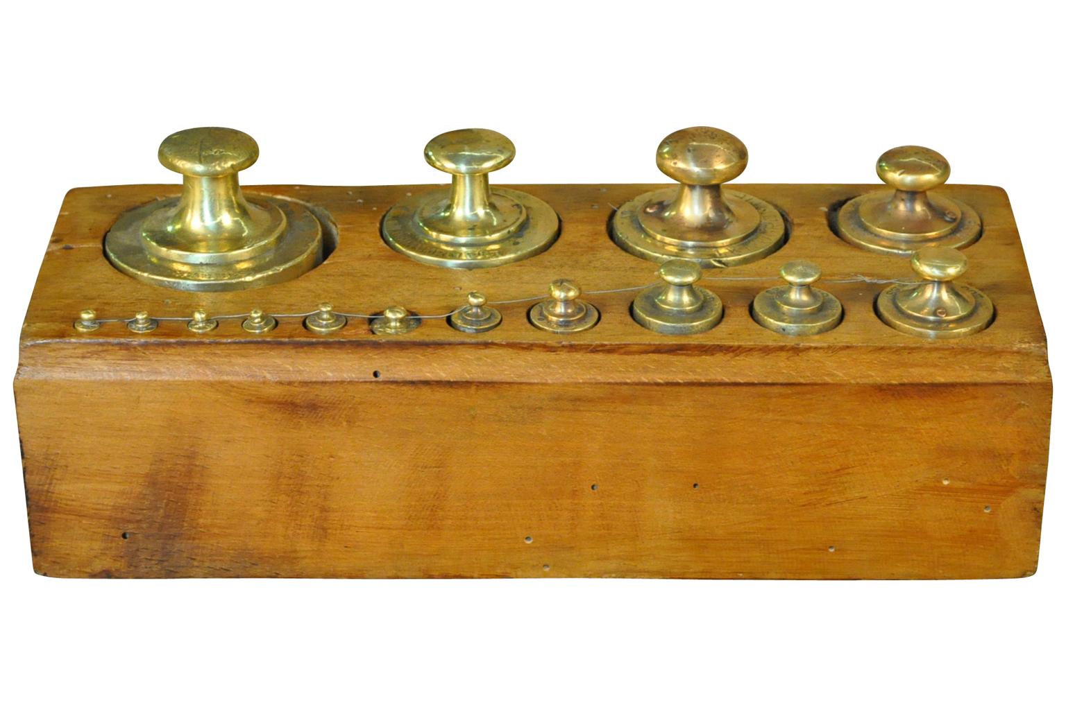 A later 19th century set of weights in brass housed in their wooden box. Weights such as these were used with different scales - balances - whether for apothecary, jewelers, confectionery, grocers. A charming accent piece for a kitchen island,