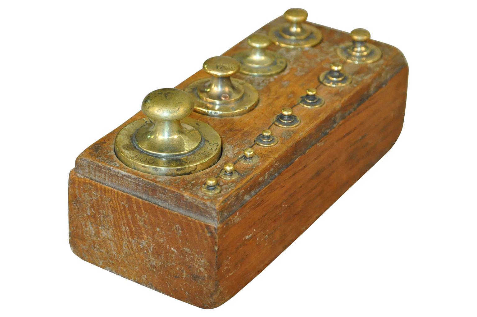 A later 19th century set of weights in brass housed in their wooden box. Weights such as these were used with different scales - balances - whether for apothecary, jewelers, confectionery, grocers. A charming accent piece for a kitchen island,