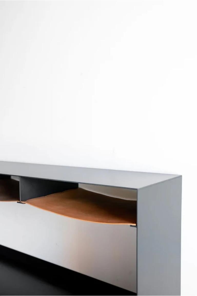 The Latigo Console features an industrial steel body with natural markings and imperfections, giving it a unique character that can only come from handcrafted design. The three shelves are made from neutral-toned vegetable-tanned leather, adding