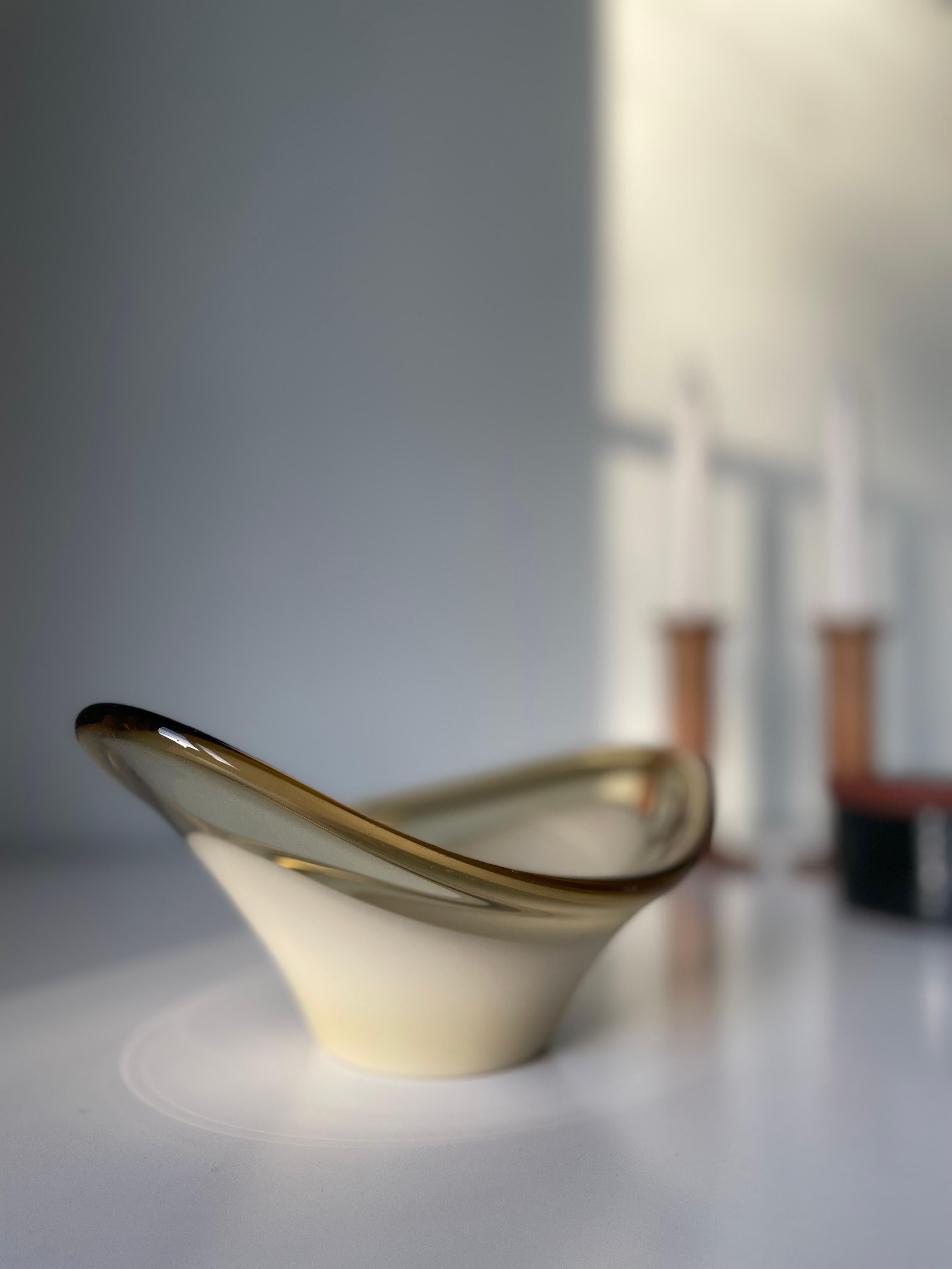 Mouth-blown modernist art glass piece from the 1960s. Smooth asymmetrical decorative vide poche bowl attributed to Danish Holmegaard. Latte color encased in clear glass with a slight smoky golden tint. Round base with a wing on each side of the