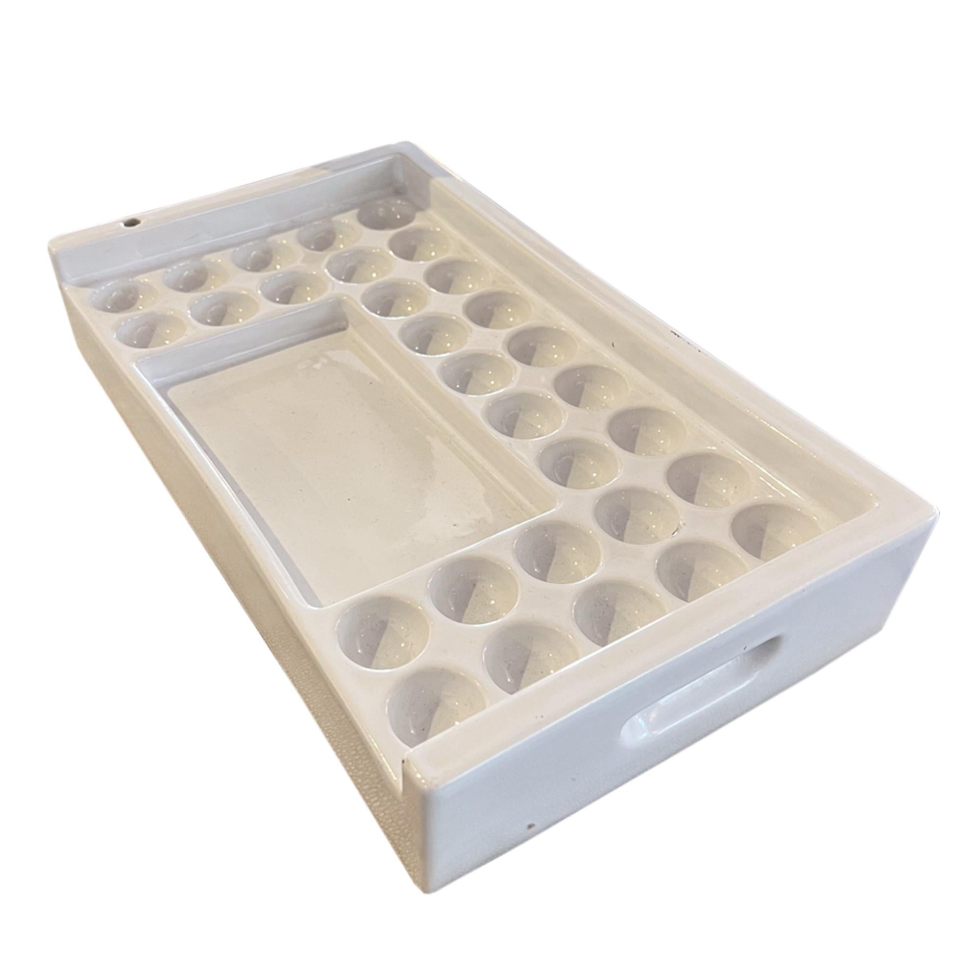 A lovely ceramic watercolour paint tray, with handles on the sides, thirty separate paint reservoirs and a mixing area. In addition it has one hole for a brush/brushes. 

Made in Switzerland in the middle of the 20th century, stamped 'Laufen' on the