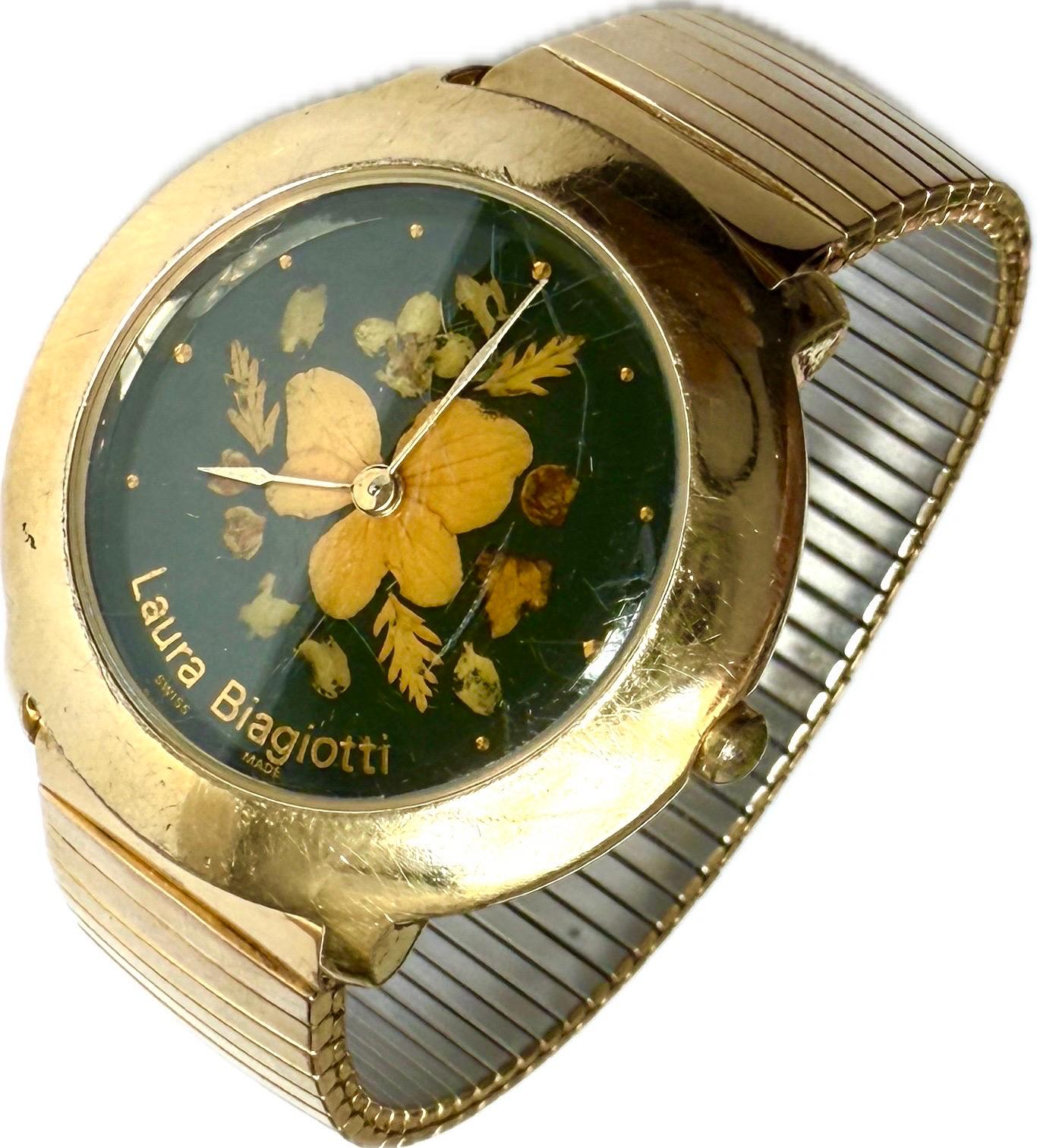 Wunderschöne goldfarbene Laura Biagiotti Damenuhr mit einem einzigartigen Blumenmuster auf dem Zifferblatt. Auf dem Ziffernblatt sind echte, gepresste und getrocknete Blumen zu sehen, die von einer durchsichtigen Hülle umschlossen sind, so dass
