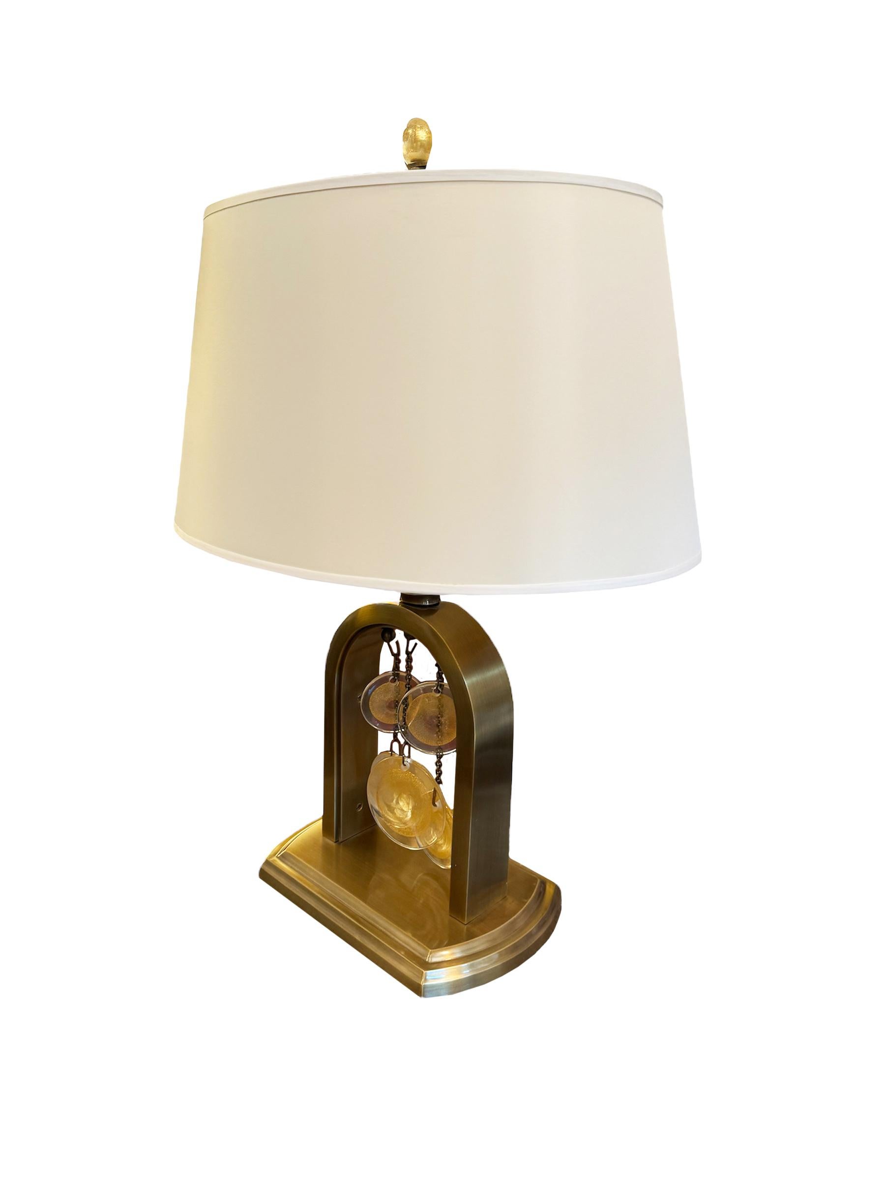 Eleva i tuoi interni con la lampada da tavolo Syro di Laura Kirar per Baker Furniture, un capolavoro di design contemporaneo e artigianato. La base della lampada vanta un'elegante struttura ad arco in ottone spazzolato che conferisce un senso di