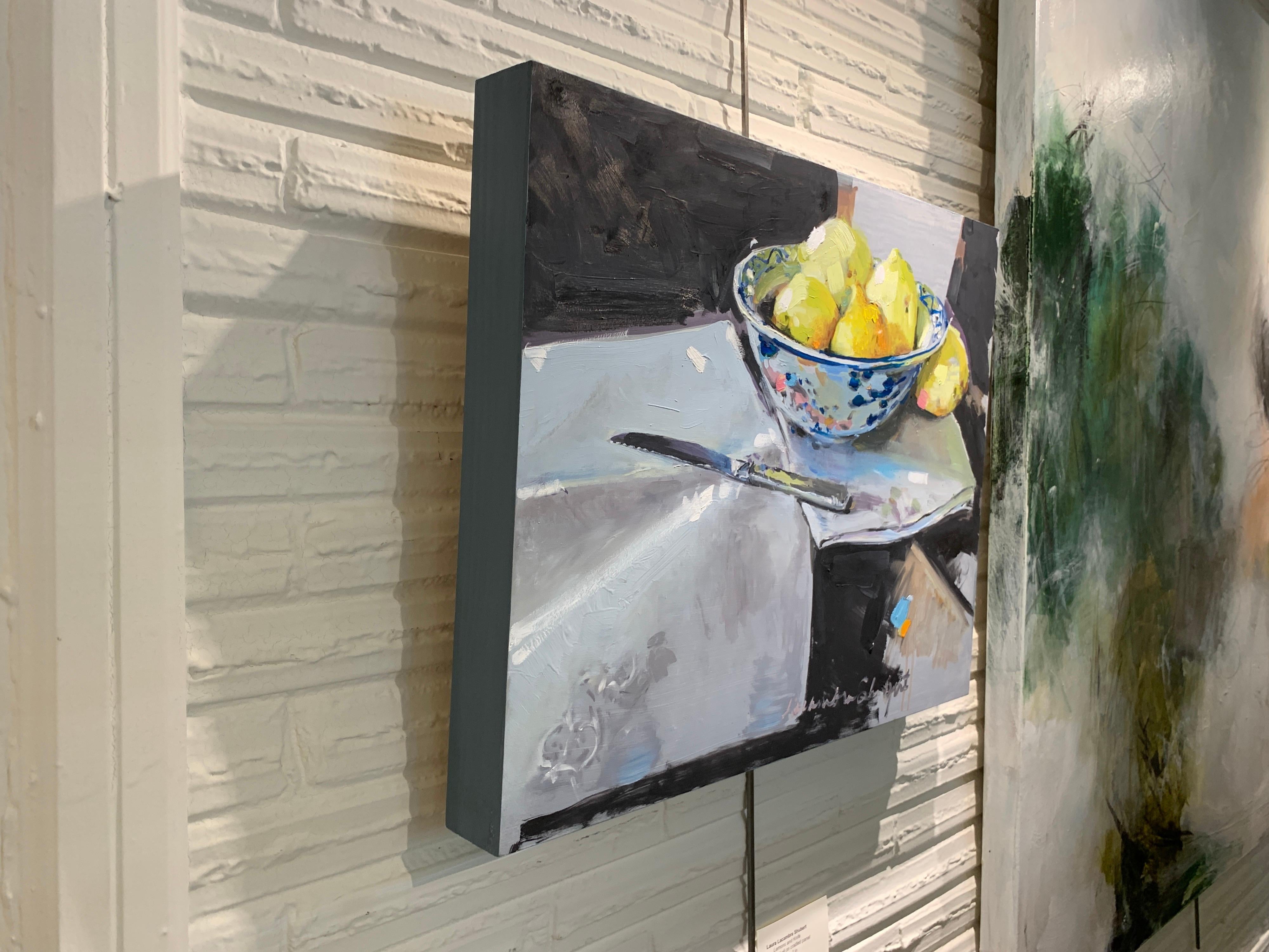 'Lemons and a Knife' est une petite peinture impressionniste à l'huile sur toile de nature morte créée par l'artiste américaine Laura L. Shubert en 2020. Avec une palette composée de tons beiges, bleus, noirs, jaunes, orange et roses, le tableau