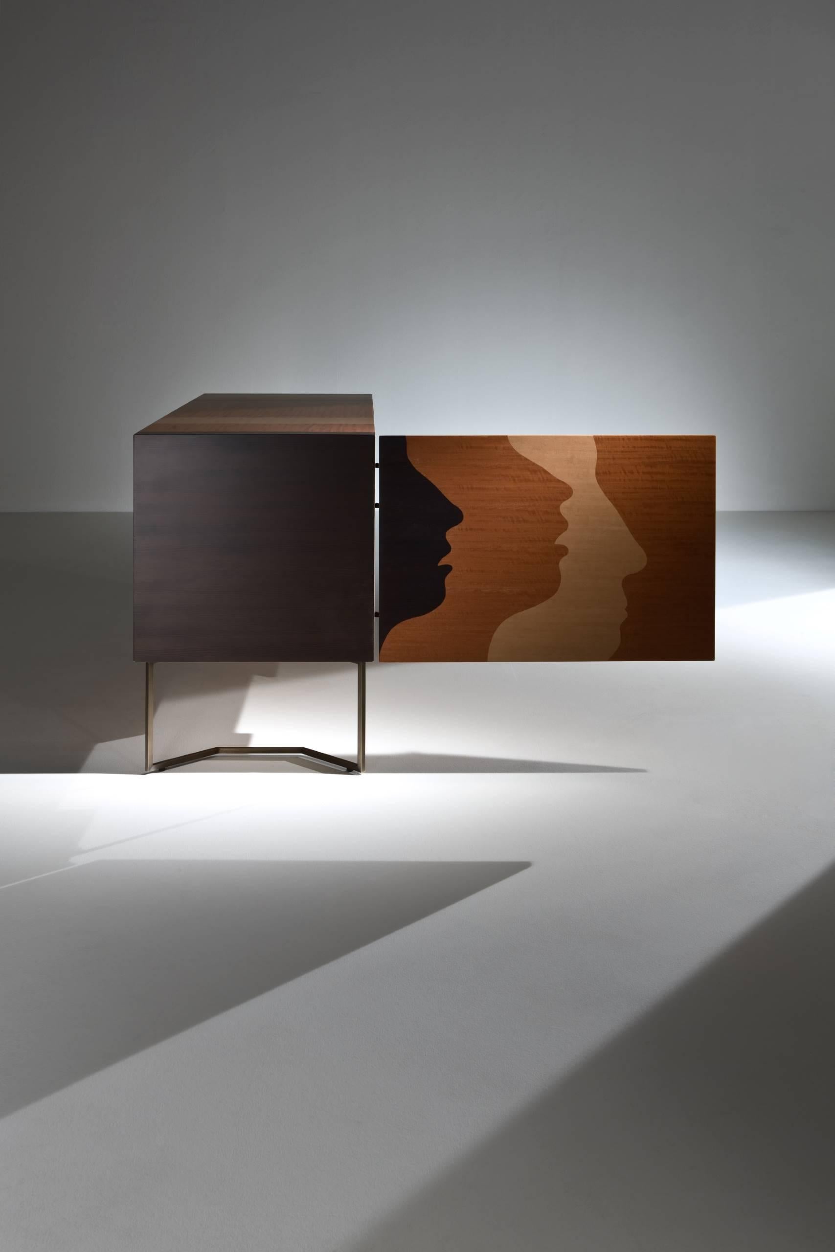 Sideboard with burnished brass legs, inlaid doors and structure. Fitted with push-pull doors, one internal shelf and two drawers.

FINISH:
Limited Edition Art Inlay

Thanks to the ancient art of wood inlays the outlines of the faces create a 3D