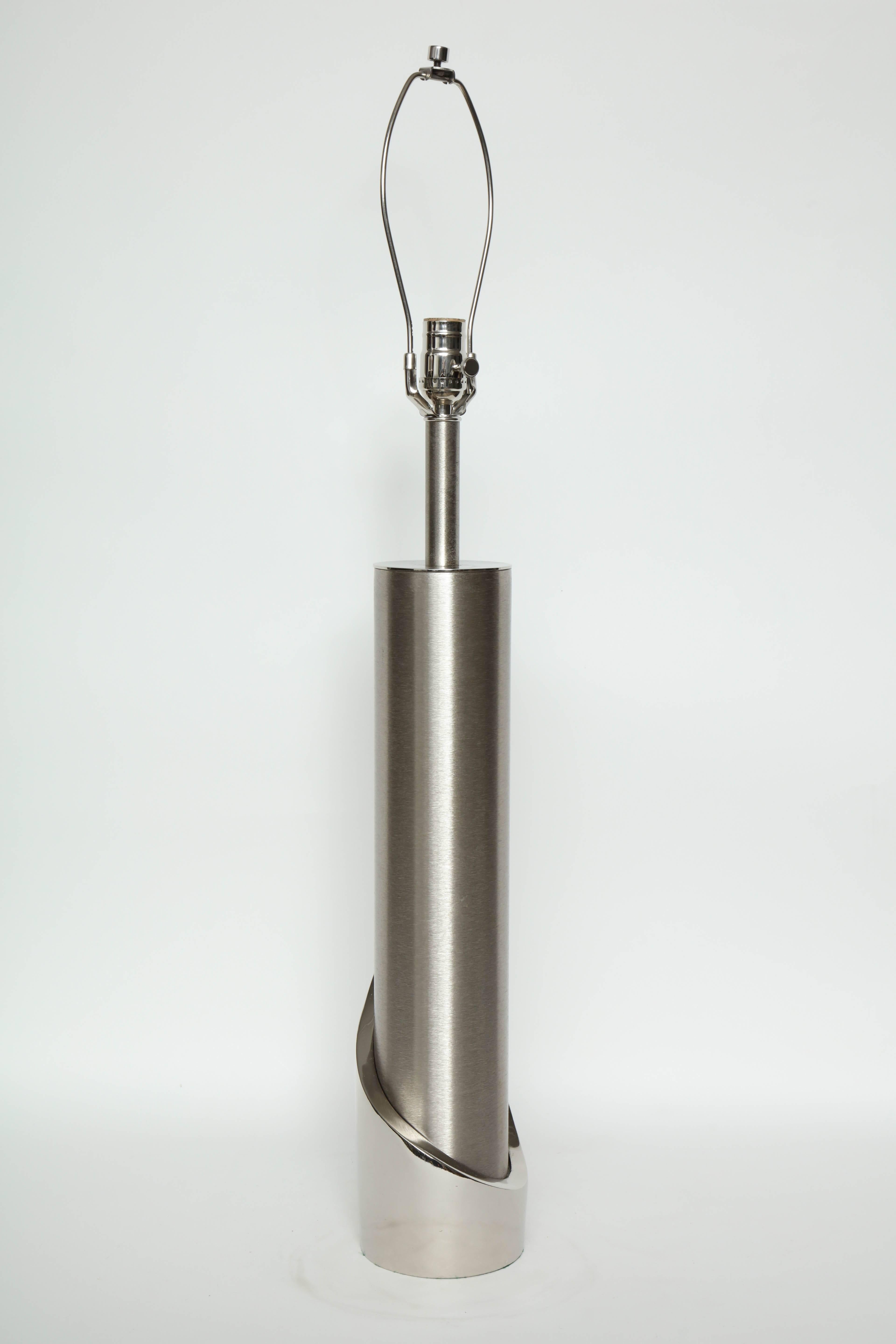 Modernist pair of brushed steel cylinder lamps accented with a polished steel base that wraps around the cylinder. Rewired for use in the USA, 100W max bulbs. Professionally polished.

Lamp body measures 20.5 inches.