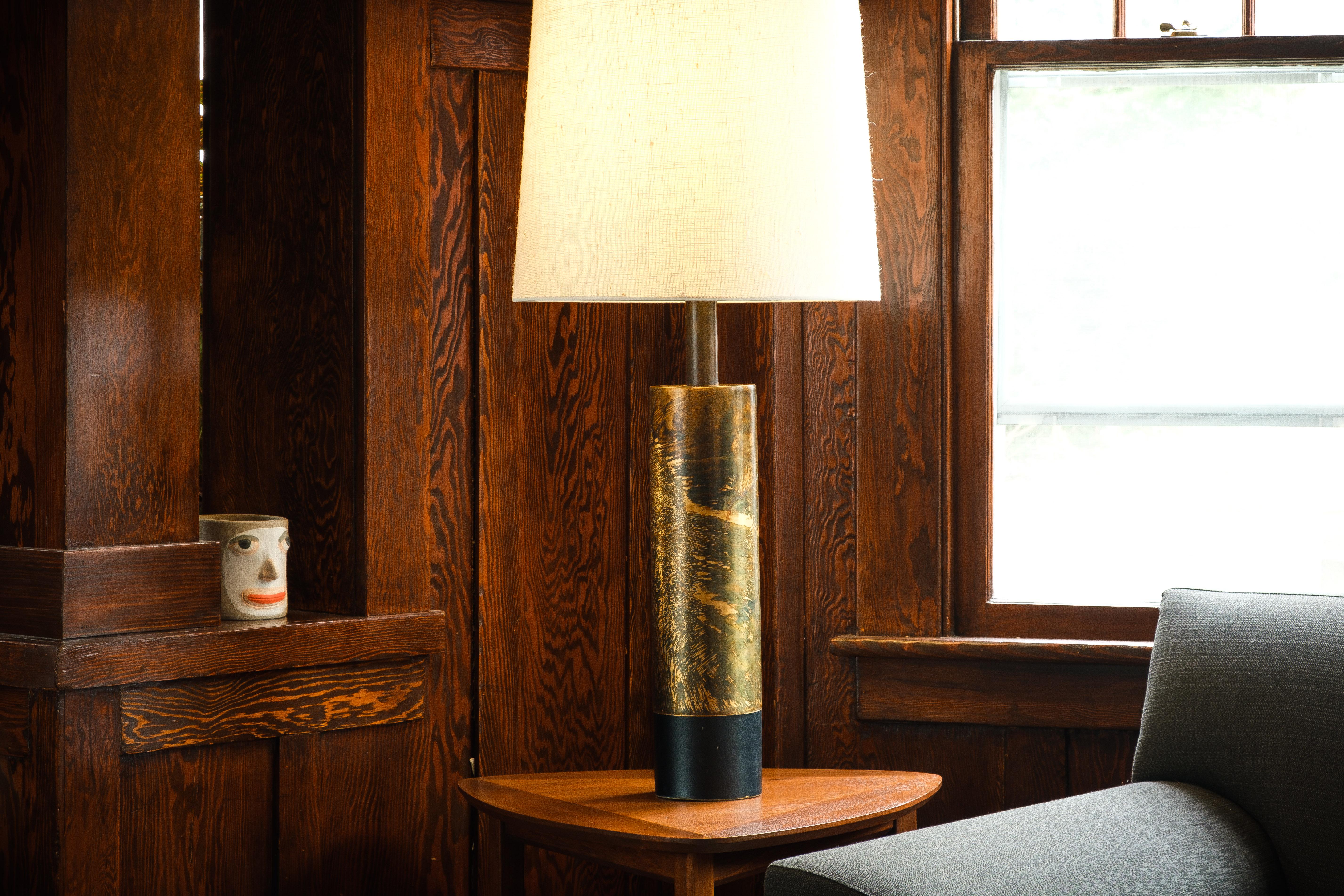 What it is 
—

This stunning Laurel Lamp Co. Lamp features an distressed, brutalist style cylindrical brass tube base with a leather cuff surrounding the bottom. Though the actual technique is unknown, the lamp was likely acid bathed to produce