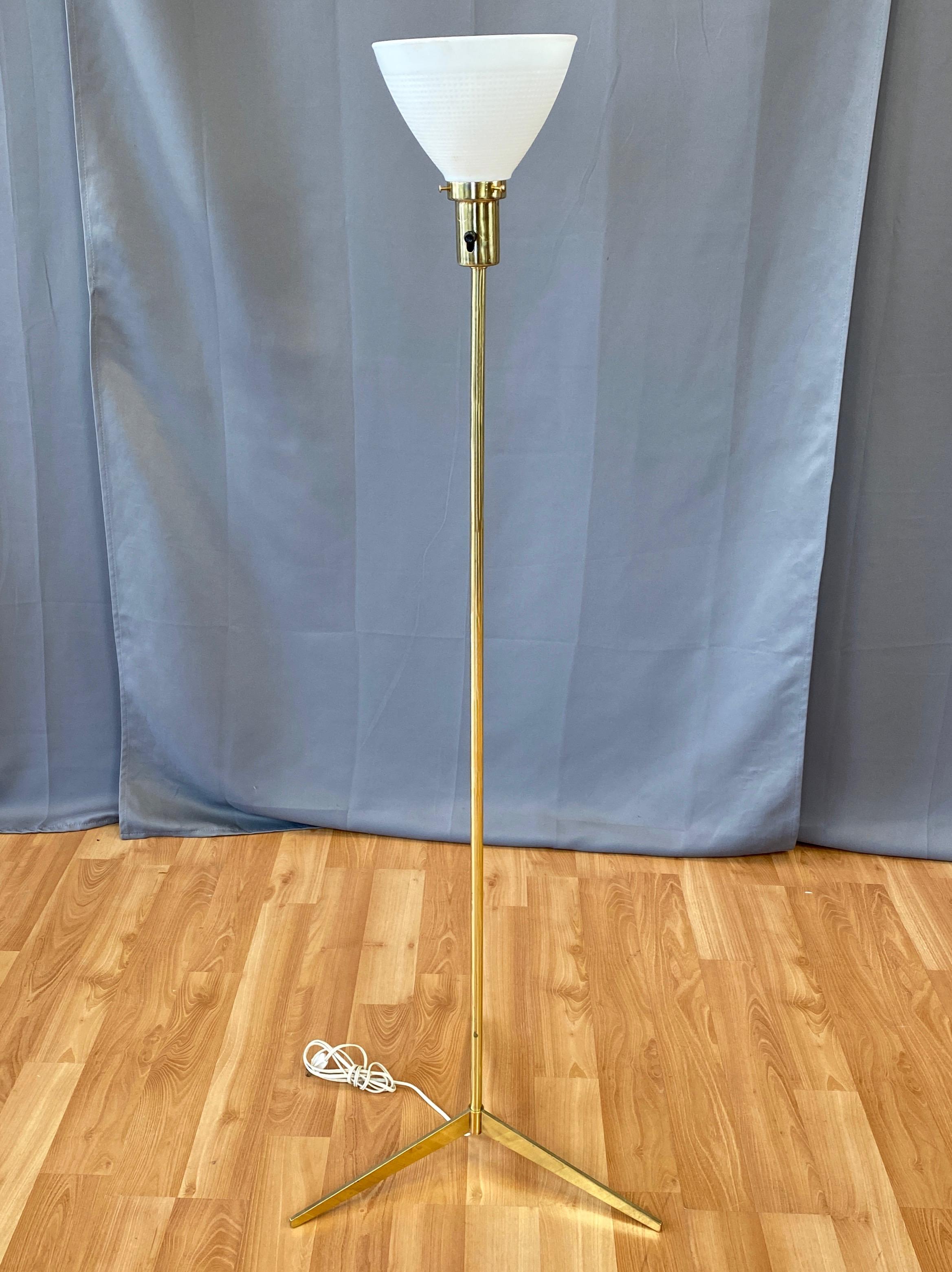 A sleek 1950s brass tripod base floor lamp by Laurel Lamp Company in the style of Paul McCobb.

Blade-like low profile three-point base in solid brass. Narrow tubular brass stem topped by a brass socket with original milk glass diffuser. Minimalist