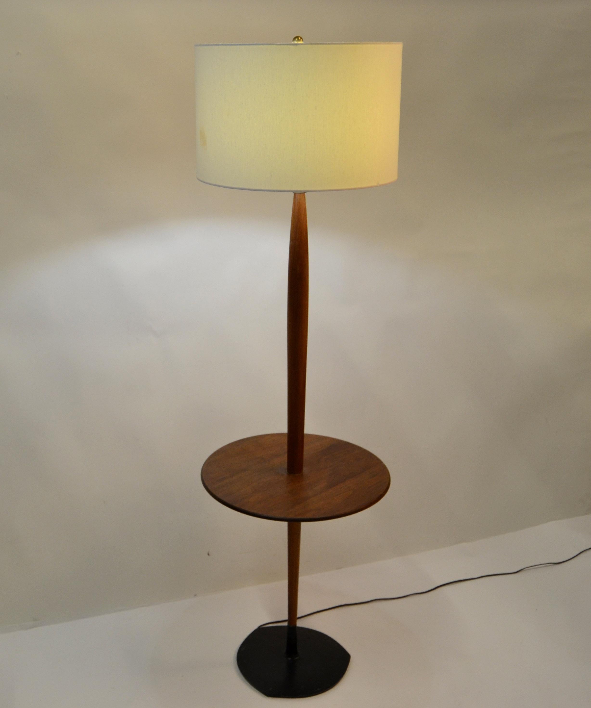 Stehlampe aus Nussbaumholz mit rundem Beistelltisch mit verjüngtem Stiel, der in den schwarzen, einzigartig geformten Stahlsockel eingesetzt ist, hergestellt von Laurel Lamp Company, ca. 1960er Jahre.
US Rewiring und nimmt 1 normale oder