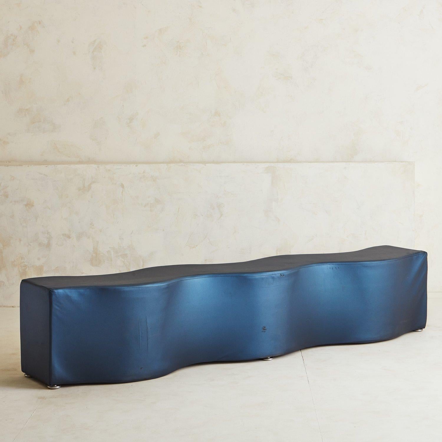 A playful curved bench featuring an organic form and original blue vinyl upholstery. This statement piece sits on four chrome feet that elevate it just slightly off the ground. Designed by Laurinda Spear for 'Brayton International.' Spear (1950—) is