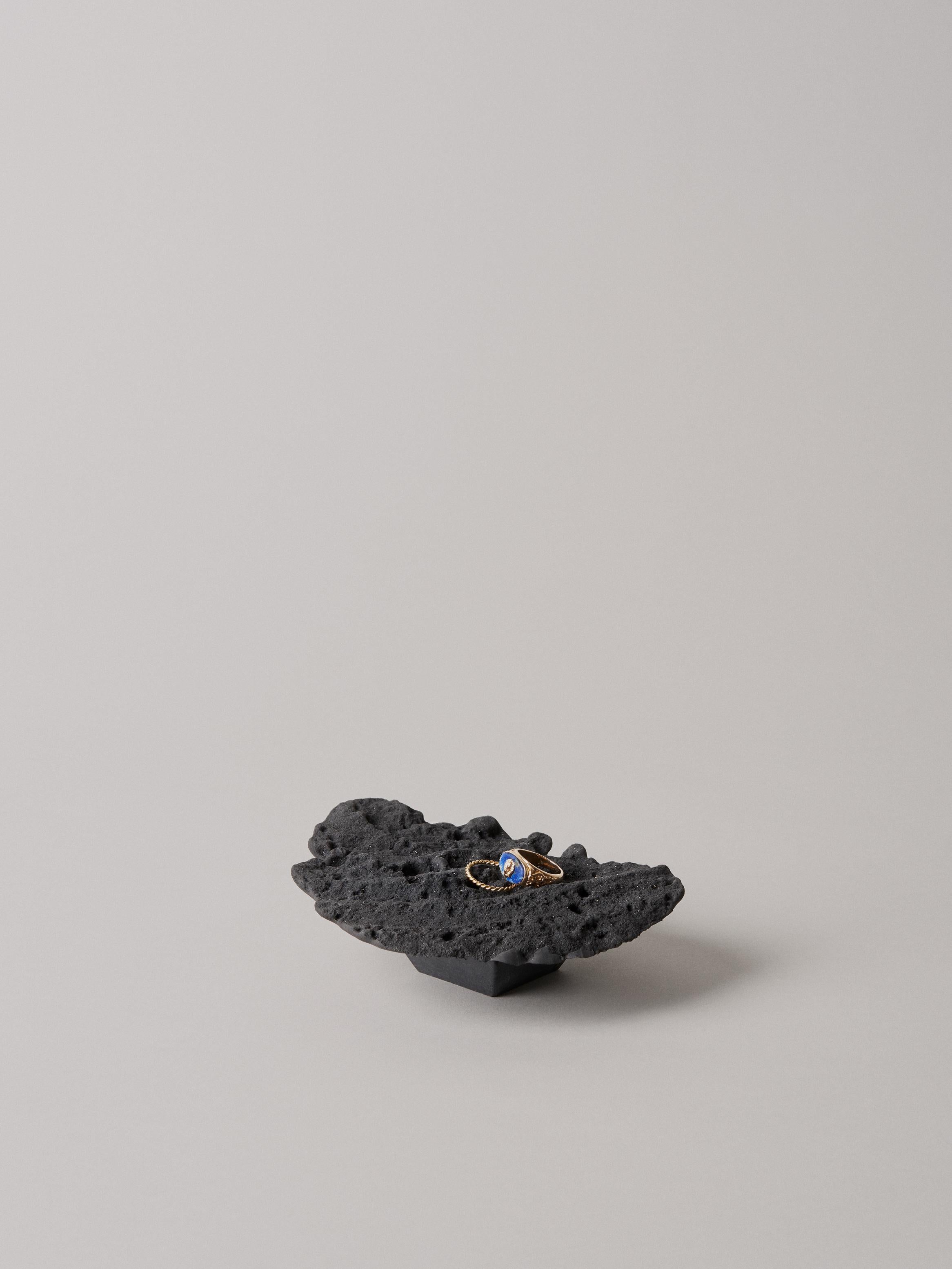 Lava bed serving plate by Kajsa Melchior
Fictive Erosion collection
Dimensions: H: Approx. 4 cm
 Ø: Approx. 40 cm
Materials: Sculpted in sand by Pressaure from air and water
 Developed in acrystal, colored by coal

This piece is also