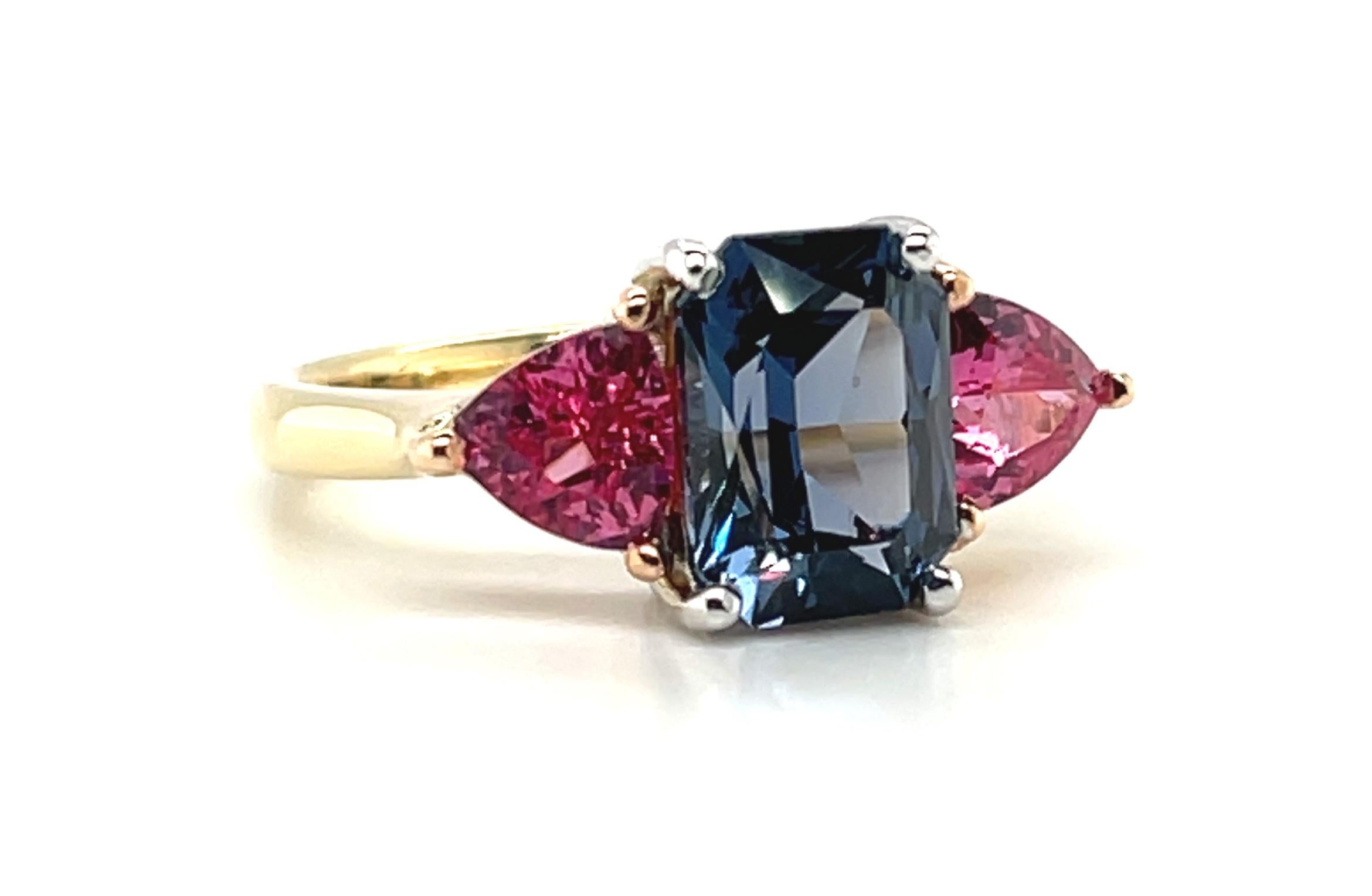 This spectacular three-stone ring features natural spinel gemstones in two vibrant colors! A 2.43 carat, gorgeous, emerald-cut lavender spinel sits front and center, flanked on either side by hot pink 