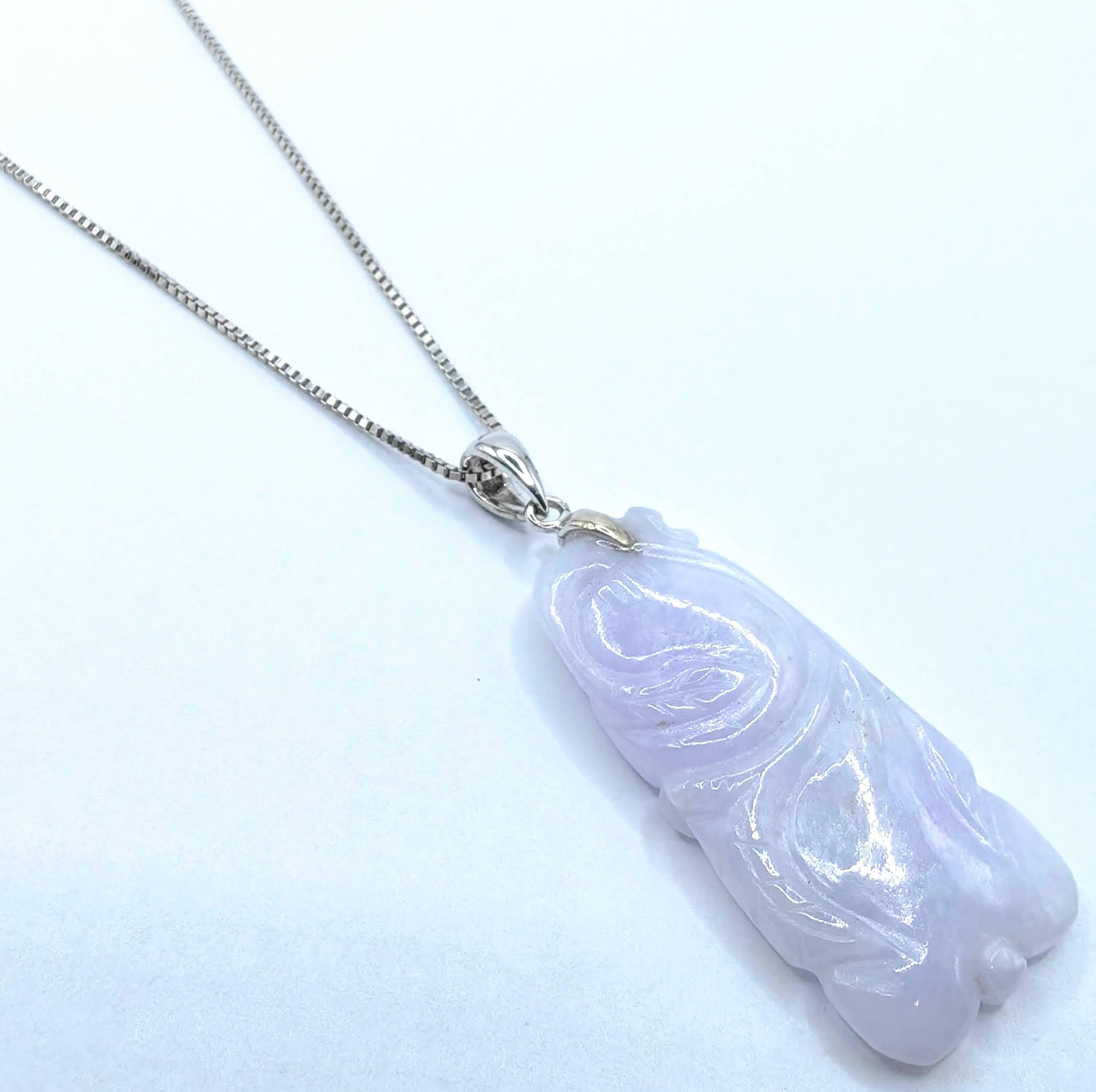 Celebra la elegancia serena con este precioso Colgante Talismán Tallado de Jadeíta Birmana Lavanda en Oro Blanco de 18 quilates. Los tonos suaves y relajantes del jade lavanda se realzan con su superficie tallada a mano, mostrando arte natural y
