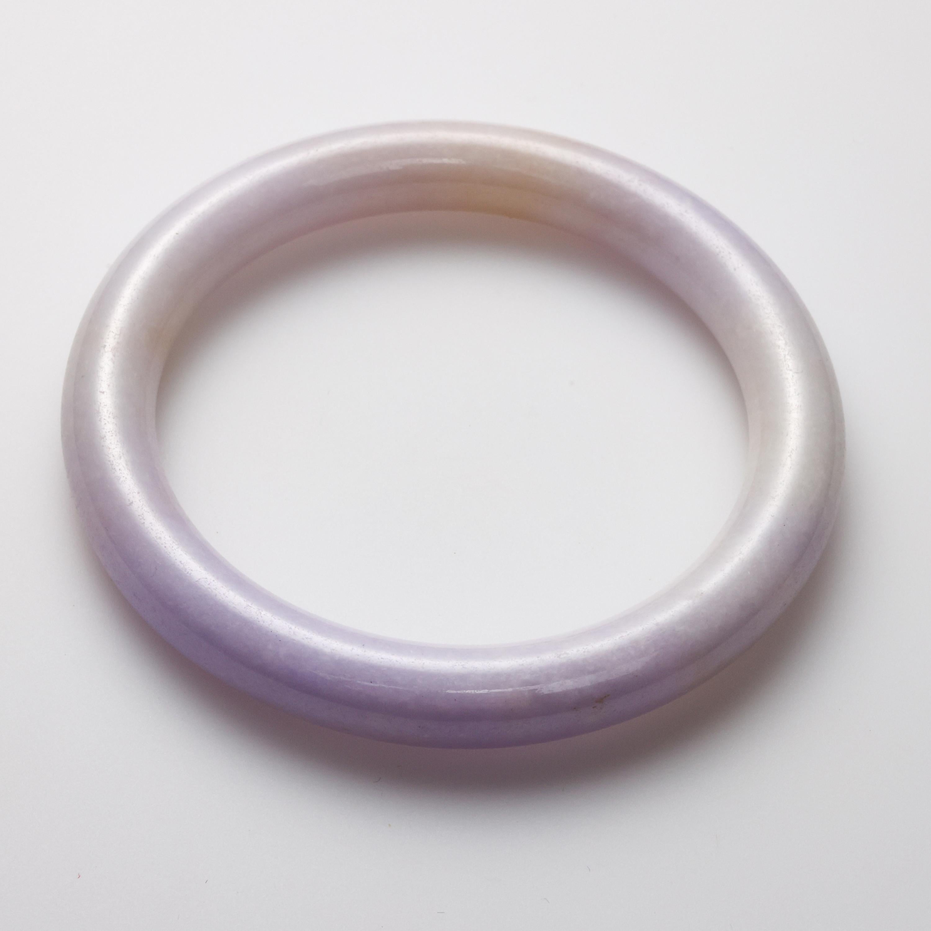 This hand-carved round, pale violet to near-colorless lavender jade bangle is luminous and ethreal. Sometimes appearing nearly white, in shadows it glows light purple. Absolutely stunning. 

Measuring 69.9 x 8.8mm, the bangle has an inner diameter