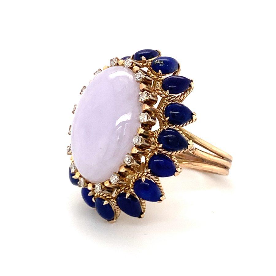 One lavender jade, lapis lazuli and diamond cocktail ring in 14K yellow gold rope motif mount centering one oval cabochon jade weighing approximately 25 ct. Enhanced by a lapiz lazuli and diamond border featuring 16 pear shaped lapis lazuli stones