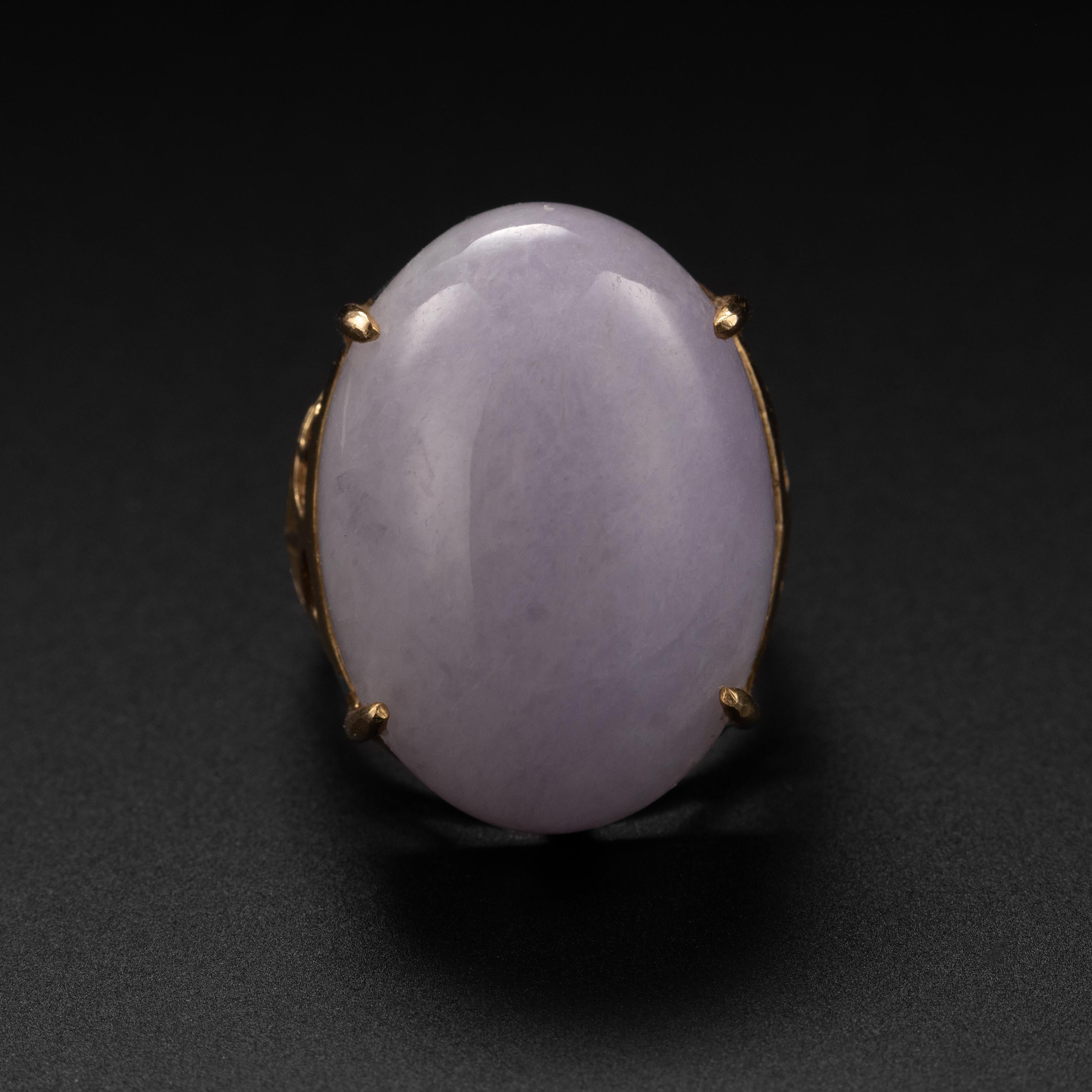 This lavender jade ring from the 1970s features an oval cabochon of translucent pale violet jade measuring 25mm x 118.8mm x 9.04mm. The impressive stone is prong-set within the hand-made 14k yellow gold setting which is marked on the interior 