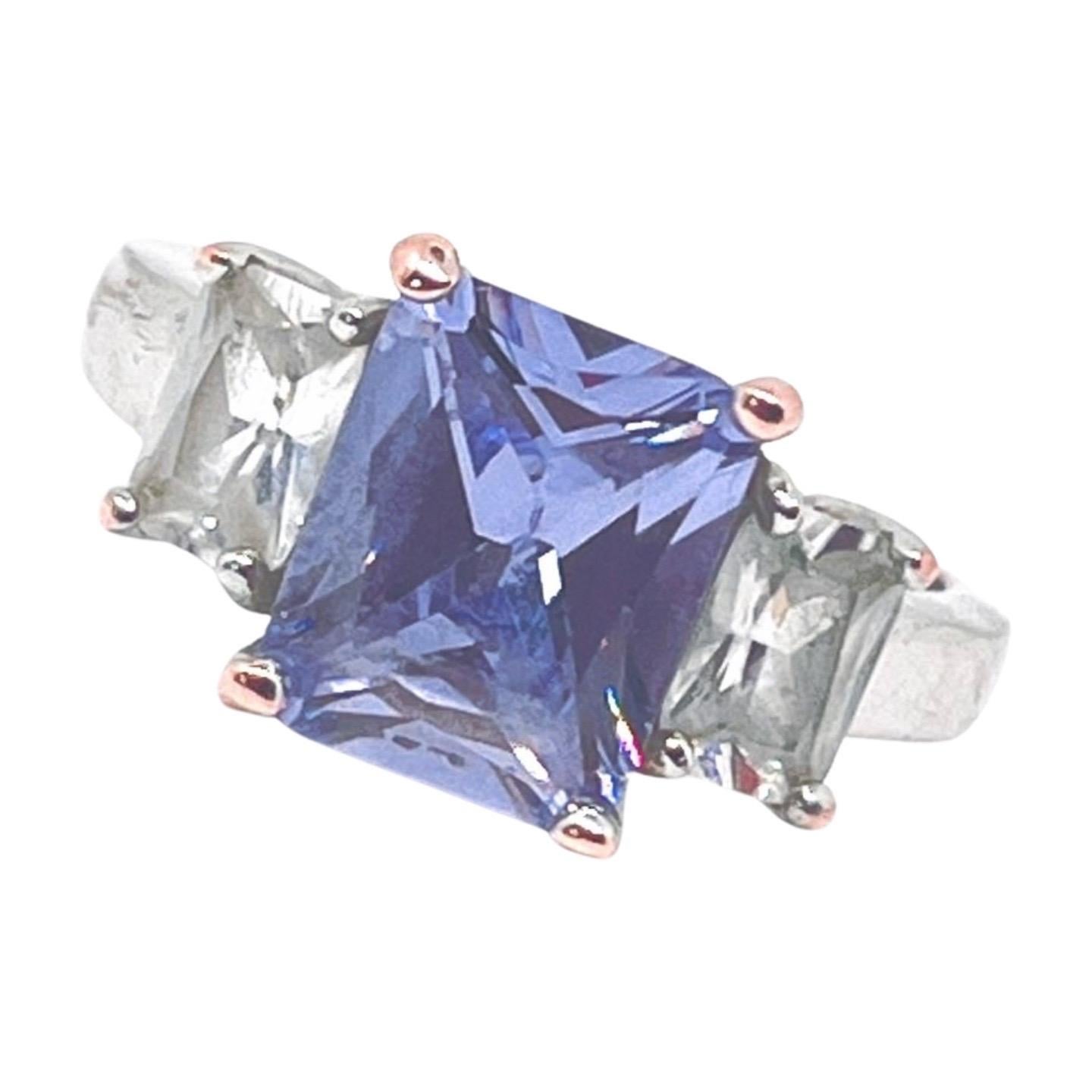 Anello con tanzanite finta a tre pietre con taglio principessa e due pietre chiare più piccole con taglio a baguette su un gambo a cattedrale. Il taglio delle pietre è splendido, ma l'usura della placcatura in ottone argentato è sicuramente