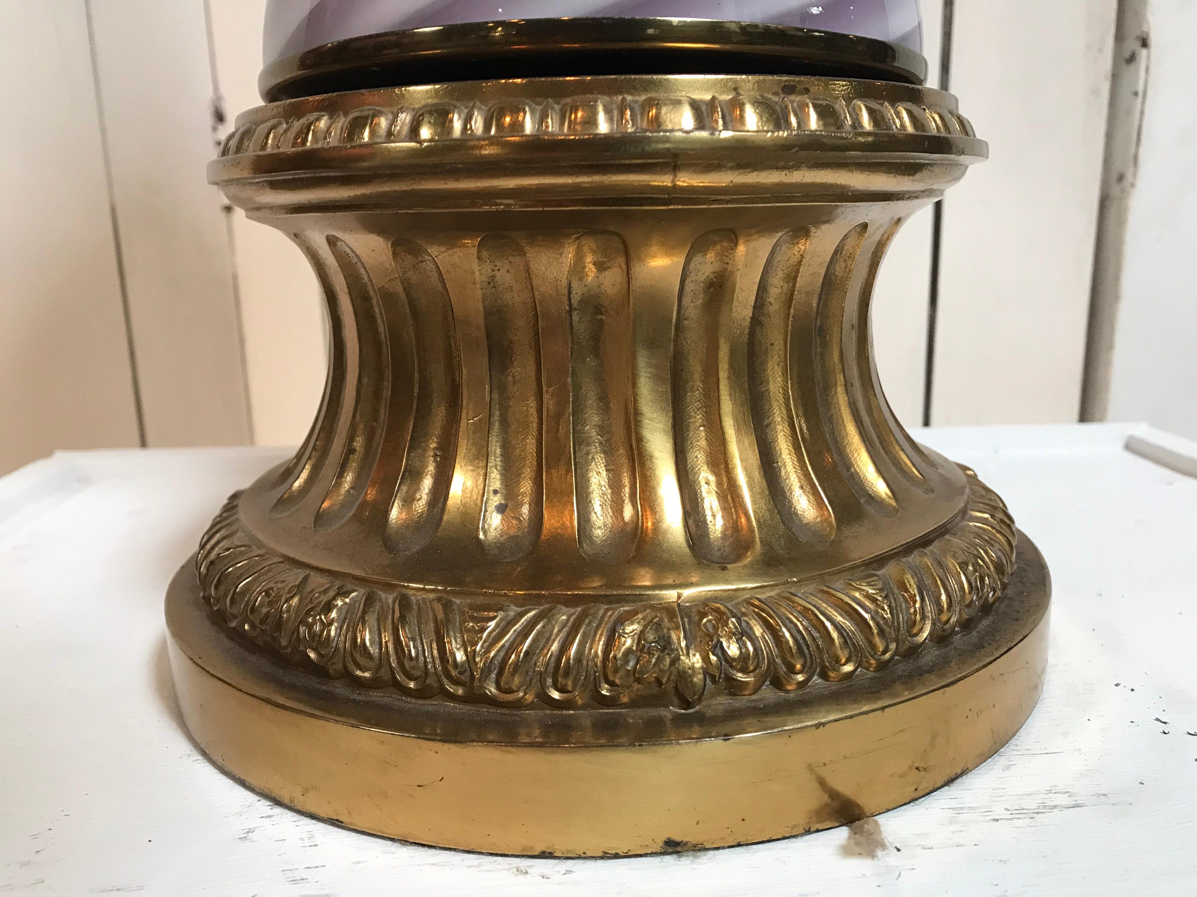 Cette lampe en verre de Murano des années 1950 repose sur une base décorative dorée, associée à un collet doré feuillu. Il présente des crêtes verticales avec des bandes diagonales lavande et blanches qui tourbillonnent jusqu'au sommet. Cette forme