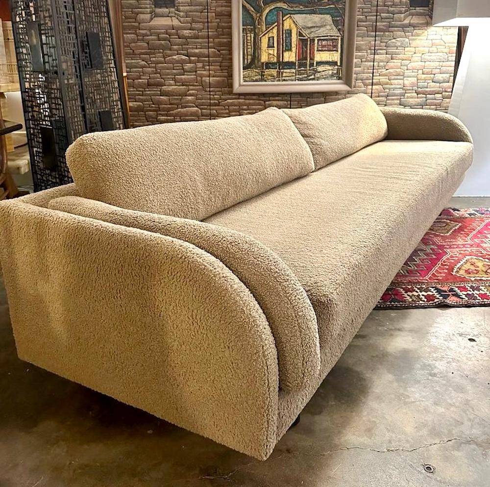 Contemporary style Lawson-Fenning Moreno Sofa in boucle sits deep and spacious with a curved silhouette, U.S., California, 2022. The sofa features a bench seat and side cushions that mimic the curvature of the arms. The back, seat and arm cushions