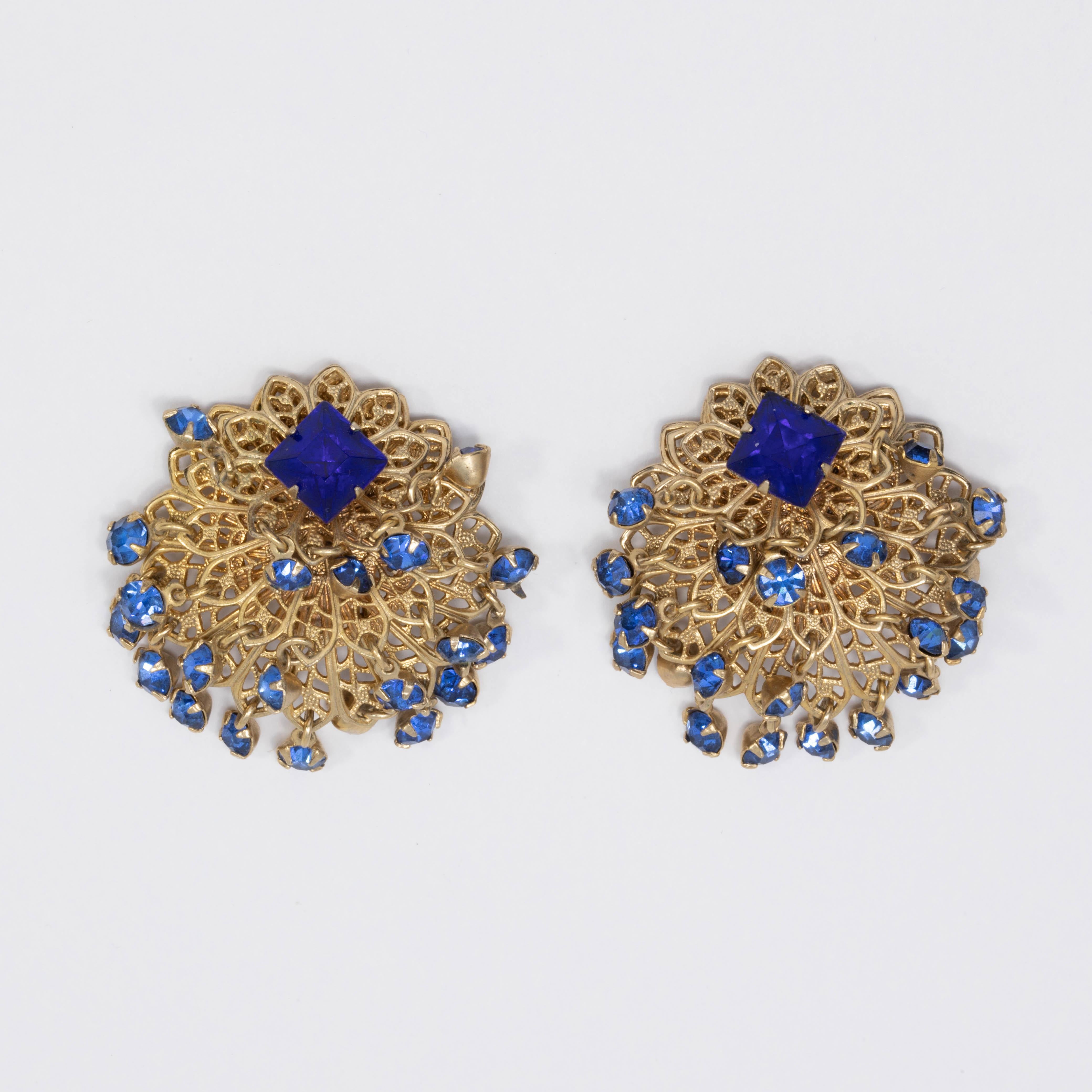 A pair of exquisite clip on earrings! Each earrings features a centerpiece square sapphire-colored crystal prong set on a layered goldtone filigree setting, accented with dangling crystals.

Hallmarks: n/a