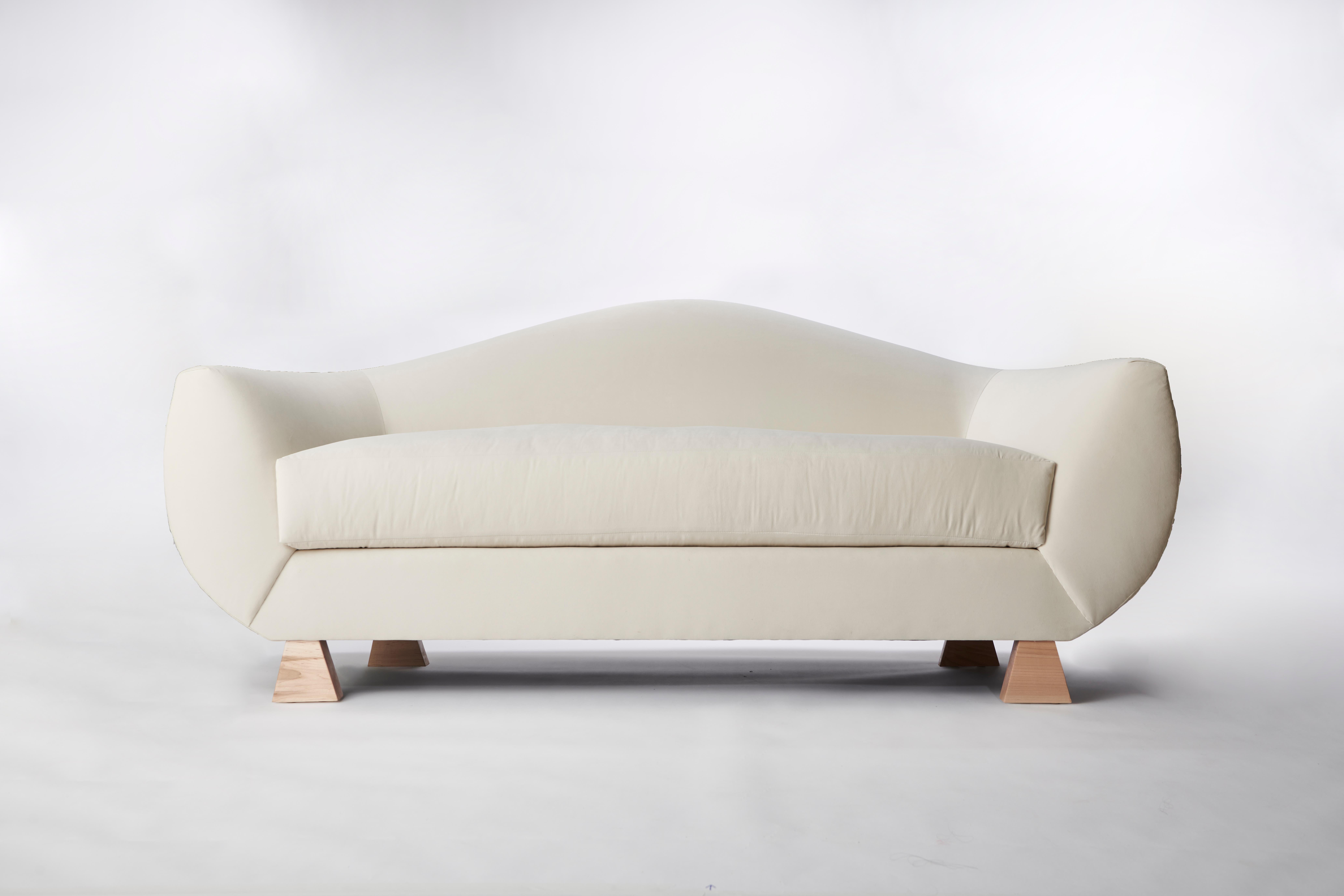 Made to order velvet and wood curved sofa designed by Christian Siriano.

Fabric: Ivory Velvet
Base: Natural Maple.
 
Available in custom fabrics and finishes.

Dimensions: 
Overall Width: 84”
Overall Depth: 32” 
Overall Height: 36.5”
Seat Height: