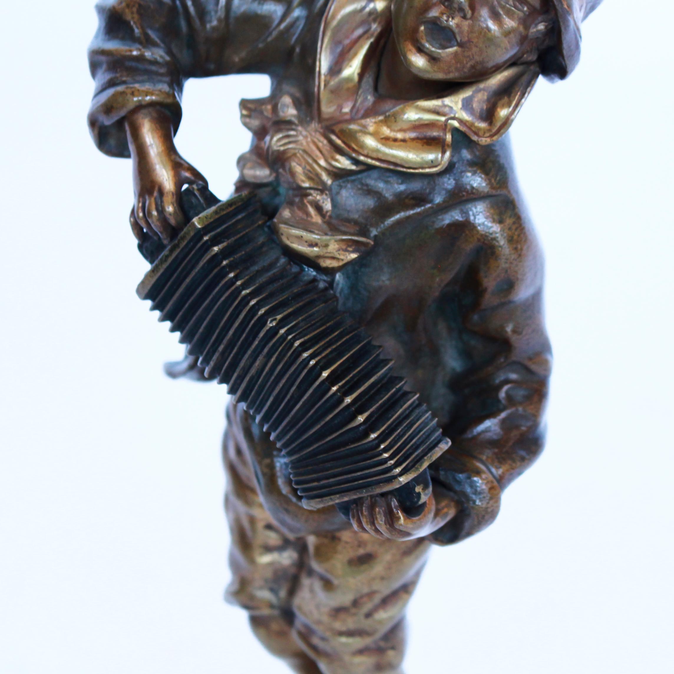 An Art Deco gilt and enameled bronze figure of a young boy playing the accordion, raised on a variegated onyx plinth. Signed 