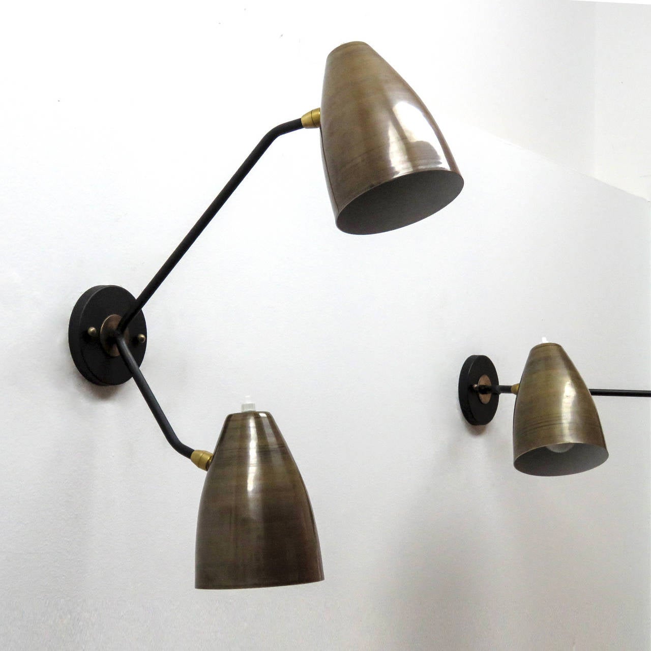 Wonderful asymmetrical double-arm wall lights by Gallery L7, handcrafted and finished in Los Angeles with two fully adjustable raw brass shades on black enameled arms, can be mounted vertically or horizontally, each shade with individual on and off