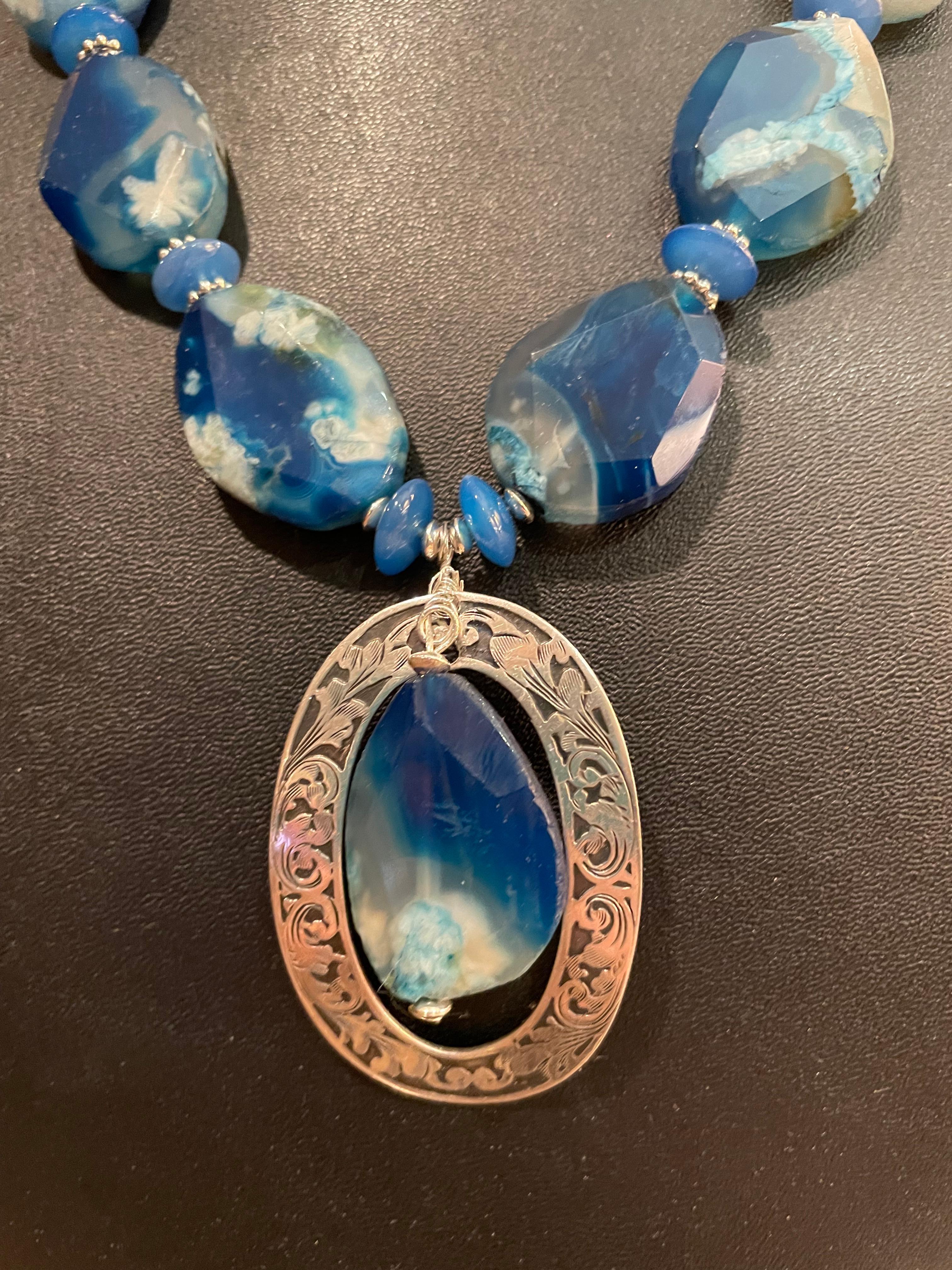 Lorraine’s Bijoux offers an impressive Blue Glass faceted necklace with a vintage Sterling Silver Brooch as the centerpiece. 
These large variegated blue glass beads include many shades of azure and sparkle due to the faceting. Each is different