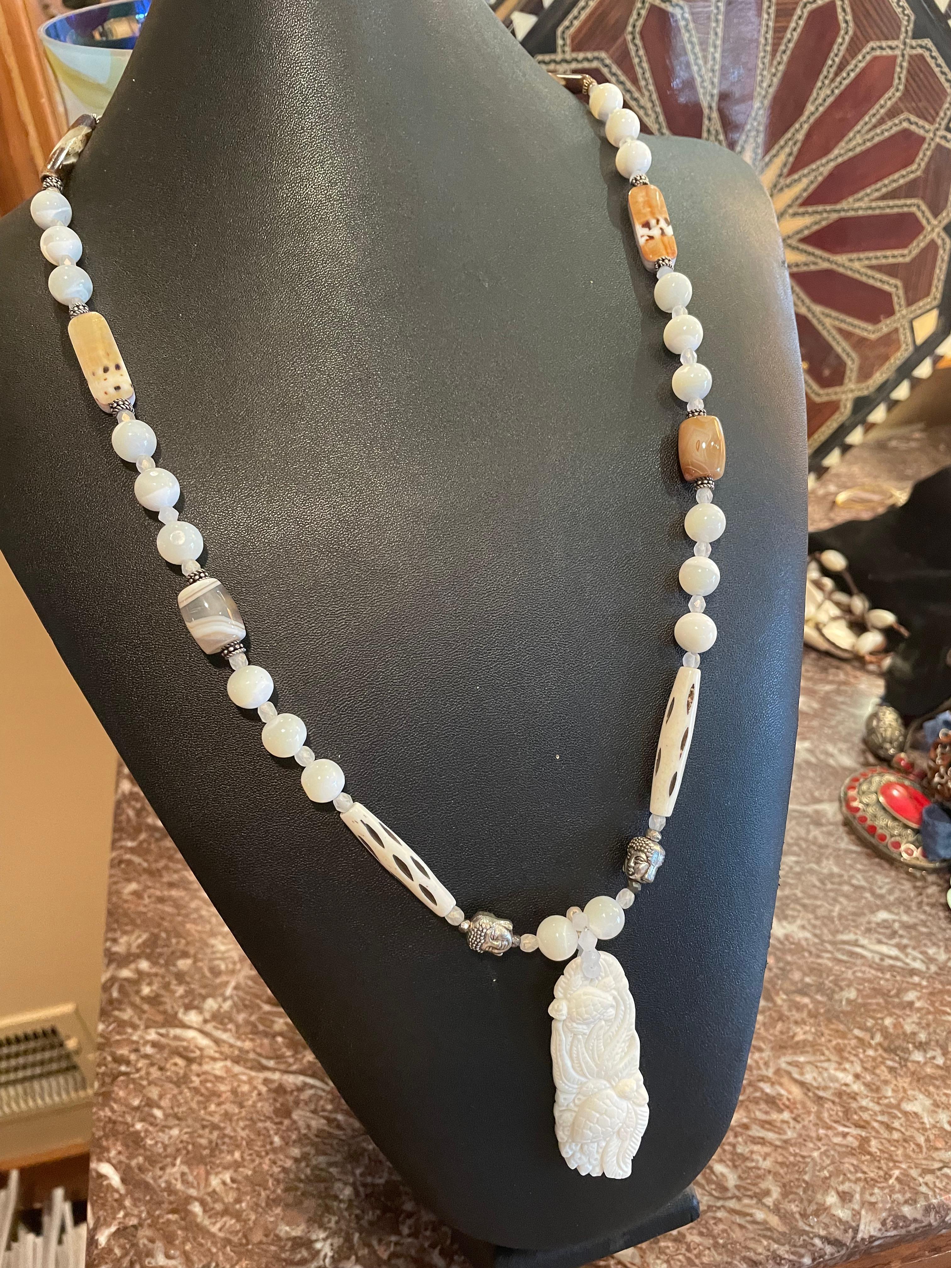 Lorraine’s Bijoux offers a handmade, one of a kind hand carved bone turtle pendant necklace.
A string of lovely round mother of pearl beads, brown agates, sterling silver Buddha head beads,and carved bone tubular beads comprise this lovely casual