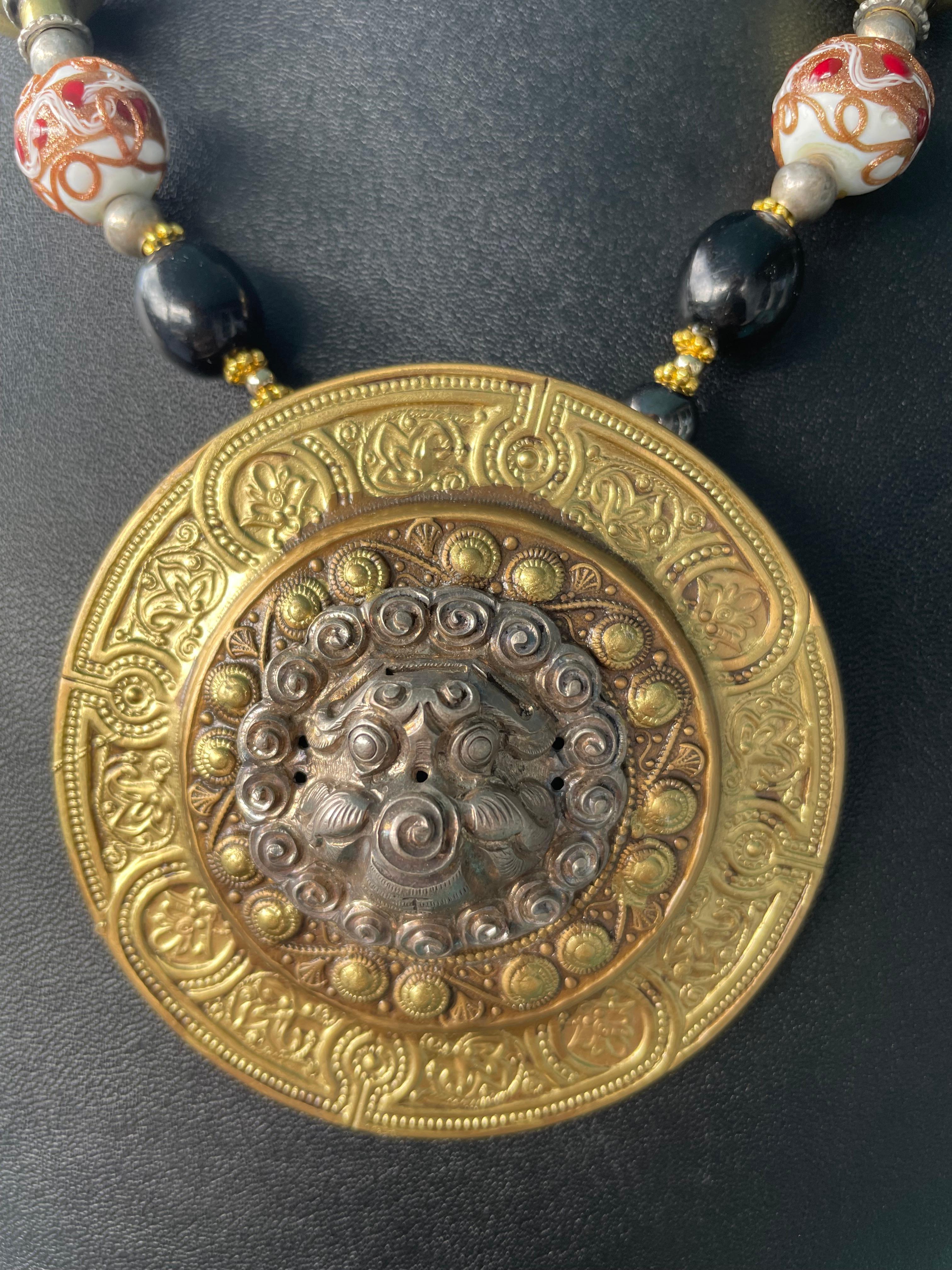 Lorraines' Bijoux propone un grande ciondolo a medaglione in ottone cesellato con al centro un leone tibetano d'epoca in argento Sterling Repousse. Perle di vetro veneziano d'epoca, corniole rotonde, grandi sfere tibetane in ottone e argento, perle