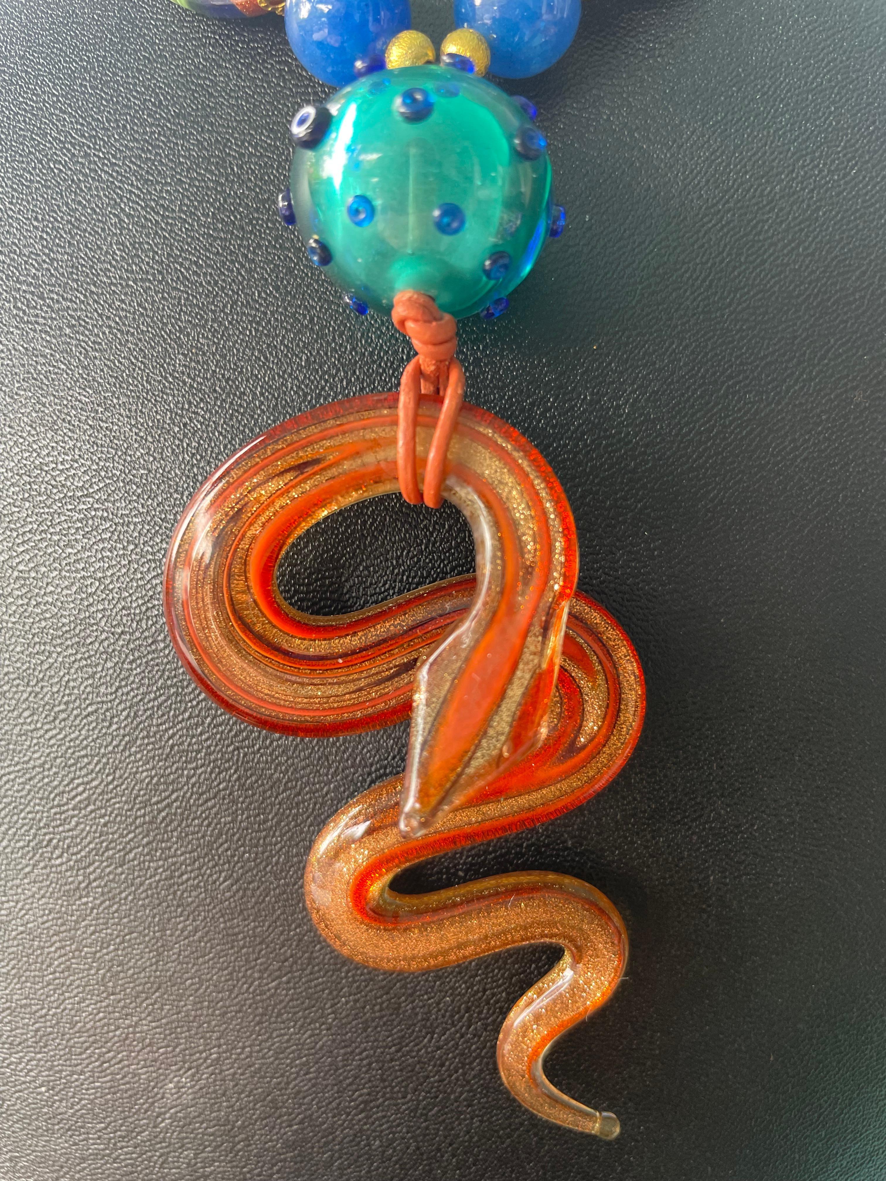 Lorraine’s Bijoux has on offer a Blown Venetian glass Serpent Pendant Necklace.
A center artist made glass bead is a one of a kind from Corning, NY. Large flat oval Venetian multi colored Mille Fiors metallic glass beads, blue agate rounds and