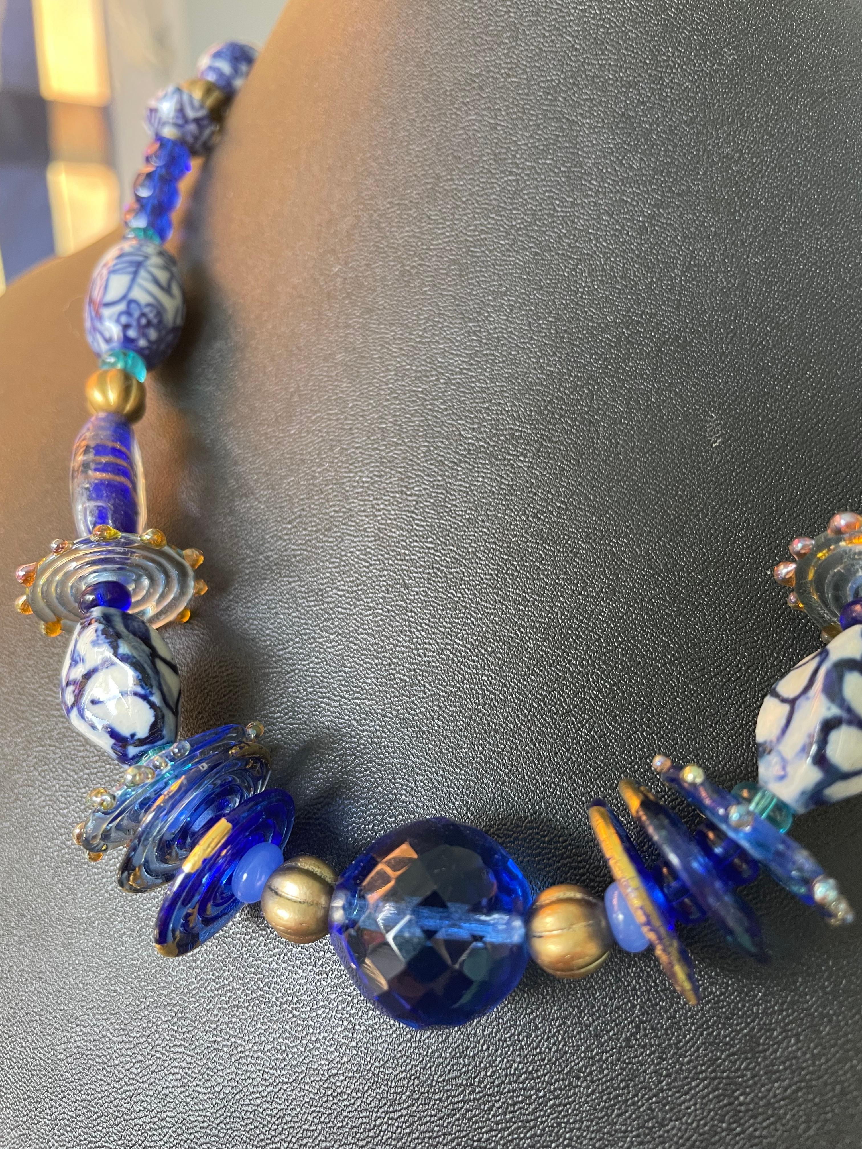 Lorraine's Bijoux propose un collier bleu composé de perles en verre faites par des artistes, de cristaux bleus vintage, de perles en verre vénitien et de perles bleues de Delft provenant de Curaçao. Des accents en laiton et des perles tchèques