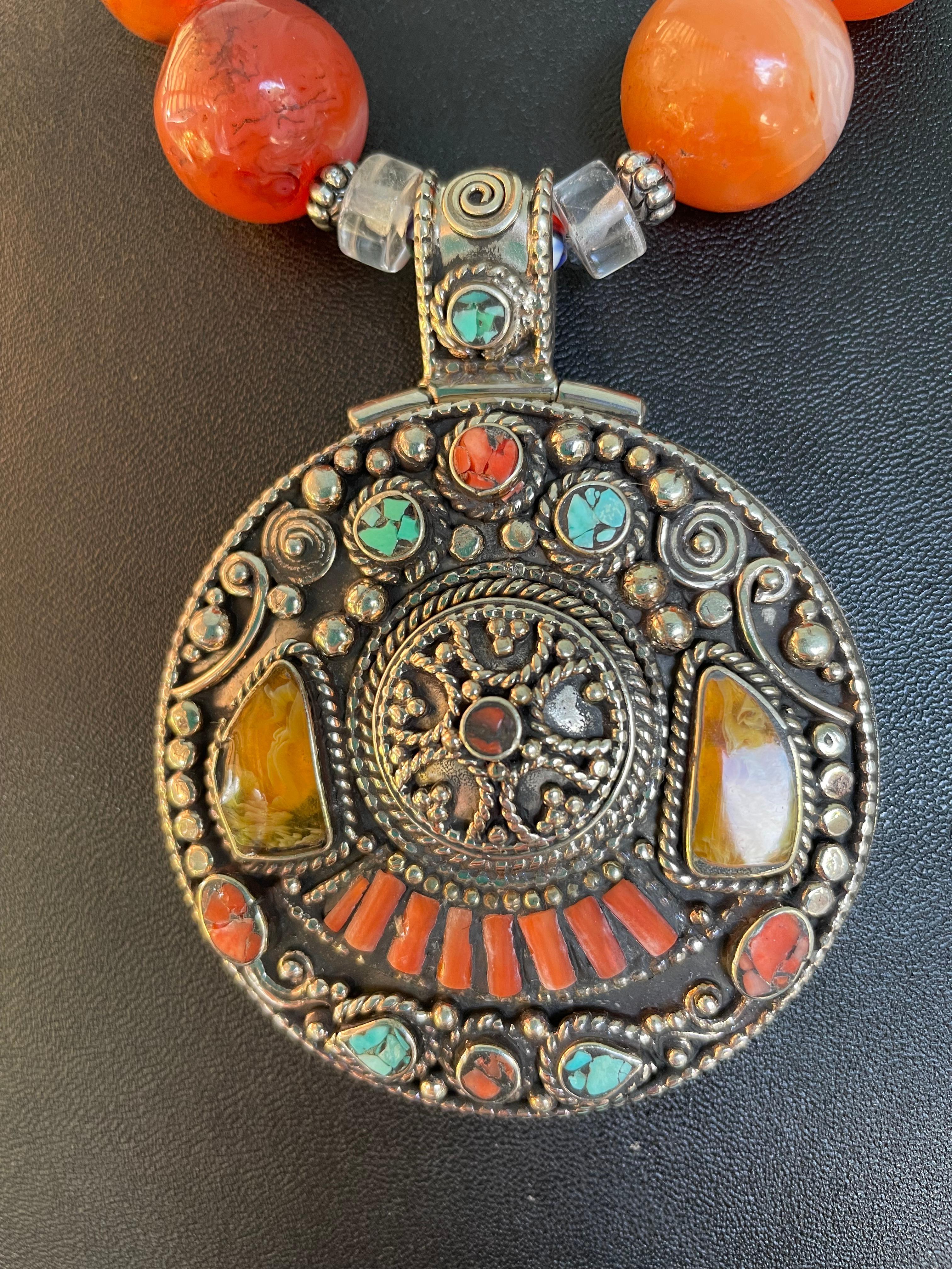 Lorraine’s Bijoux has on offer a Large Round Inlaid Tibetan amulet necklace. Amber, Turquoise, and red coral are inlaid into a magnificent silver work pendant. The string of very large Carnelian round beads, Rock crystal rondelles, Brass Tibetan